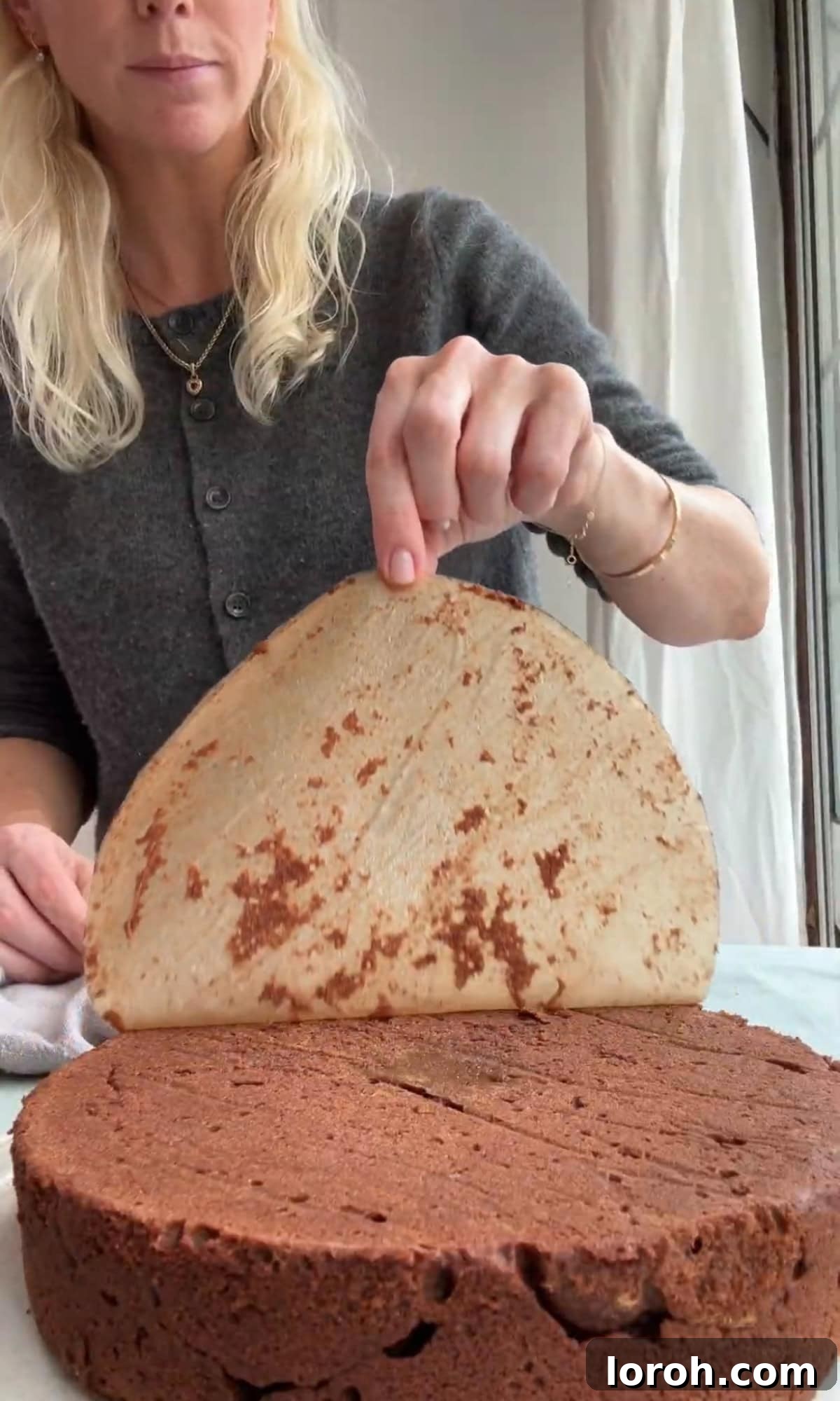 Removing baking paper from the cooled torta caprese, revealing a smooth surface.