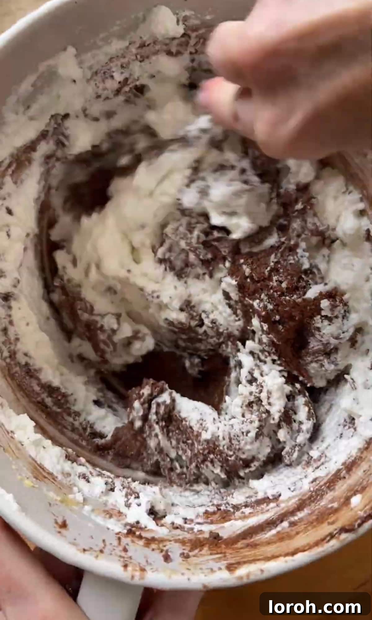 Gently folding whipped egg whites into the chocolate almond batter with a spatula.