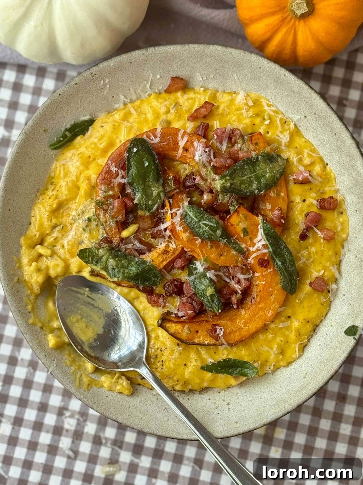 A bowl of creamy pumpkin risotto, garnished with crispy sage and pancetta, with a spoon resting in it.