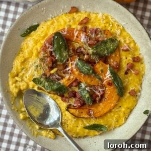 A grey bowl brimming with creamy pumpkin risotto, garnished with a sprig of sage and a spoon.
