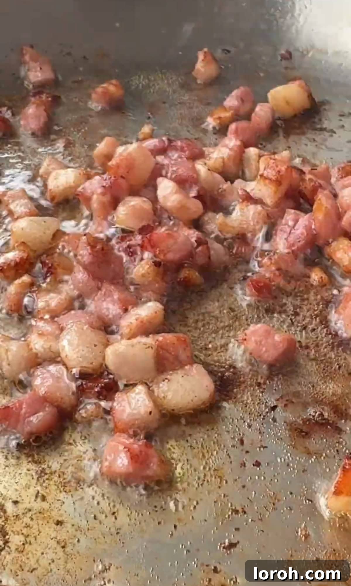 Pancetta cubes sizzling and browning in a hot frying pan.