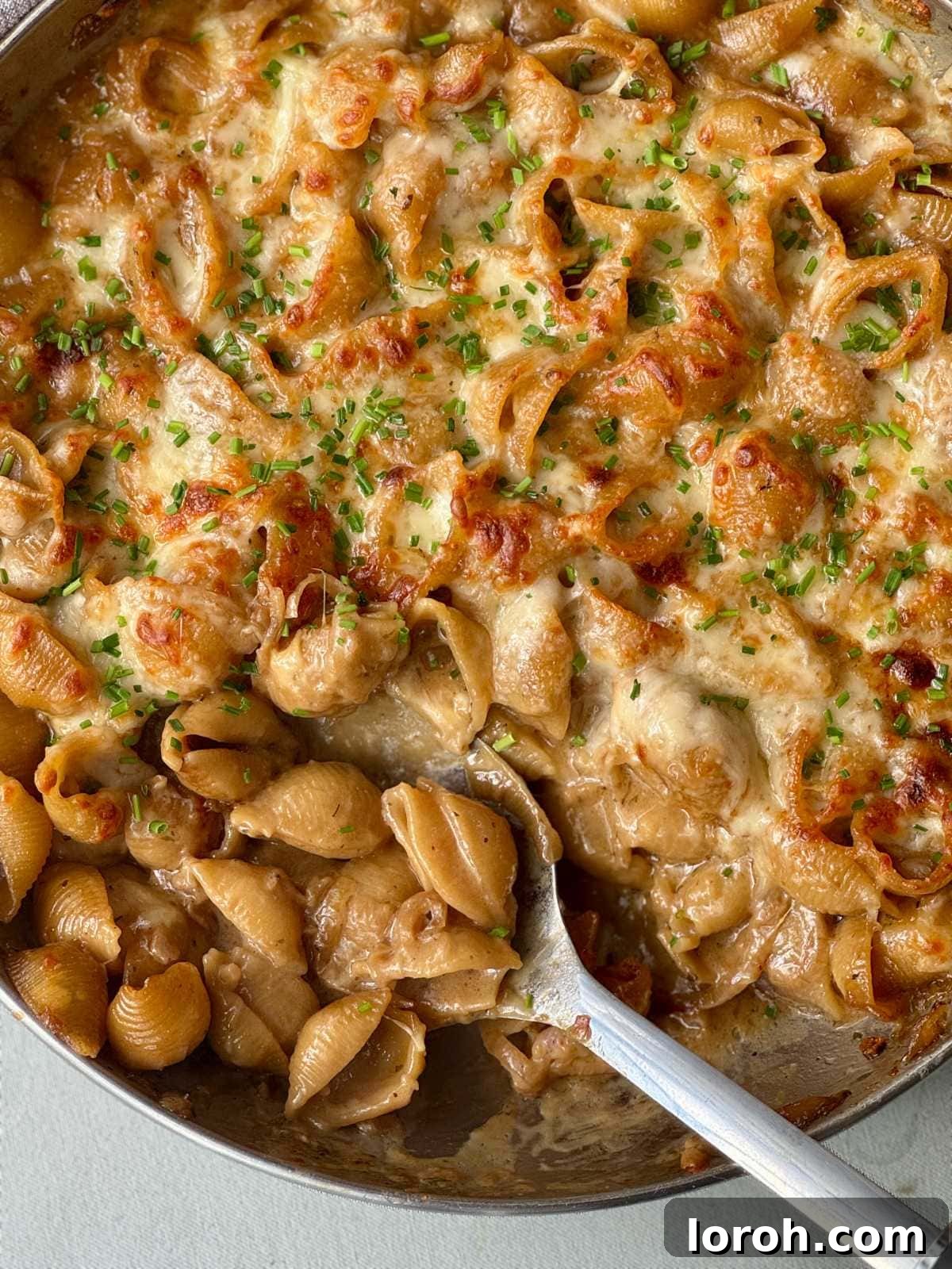 spooning french onion soup pasta. A rich, creamy pasta dish with visible caramelized onions and a golden cheesy crust.