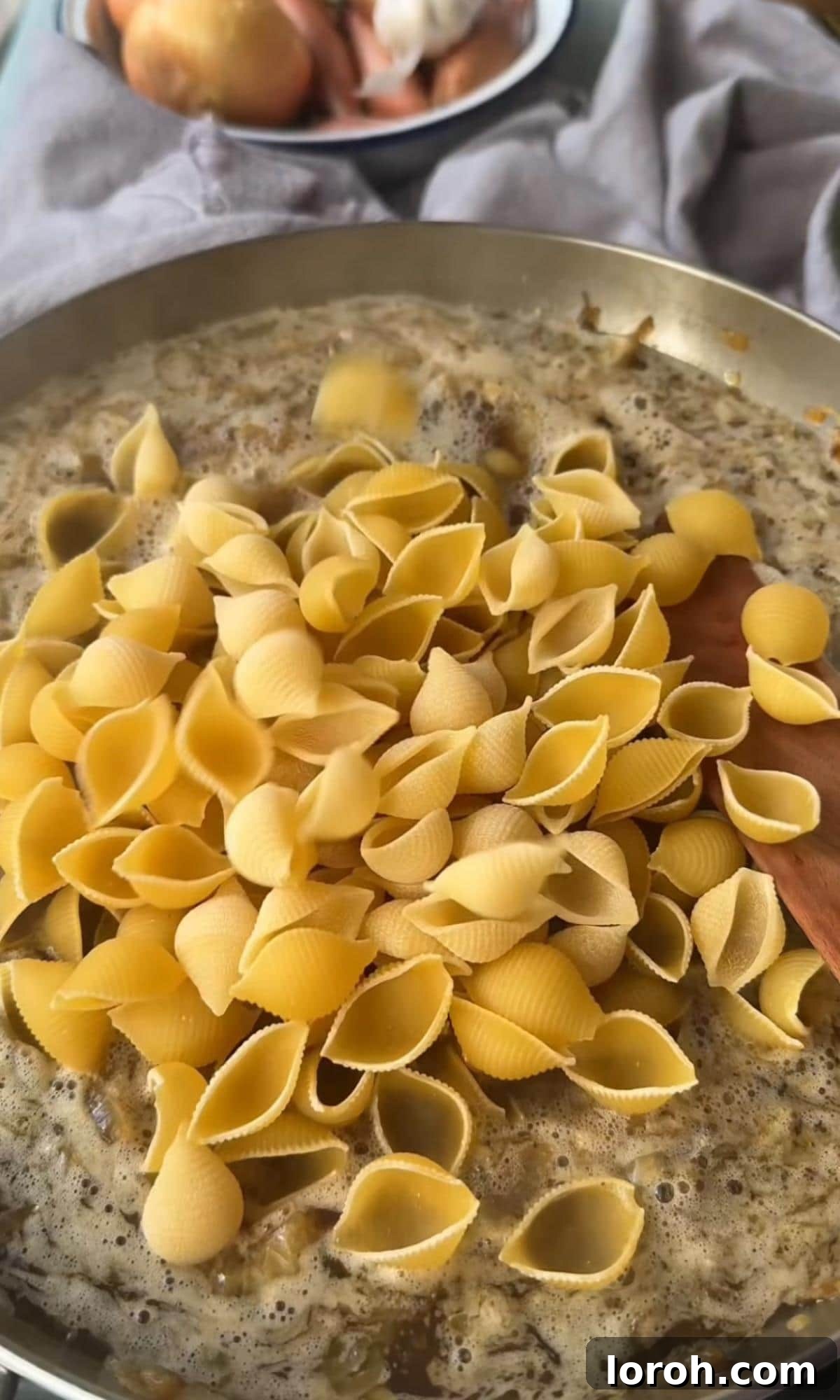 adding pasta to the french onion soup pan. Pasta mixed with onions and broth, simmering.