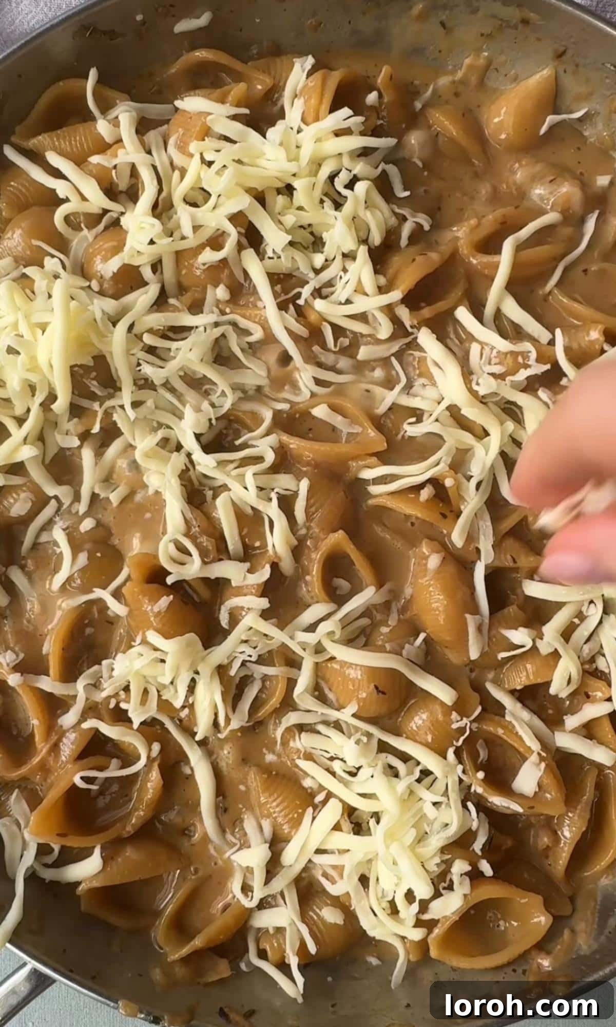 adding gruyere to the pasta. Grated Gruyère cheese being sprinkled over the pasta in a pan.