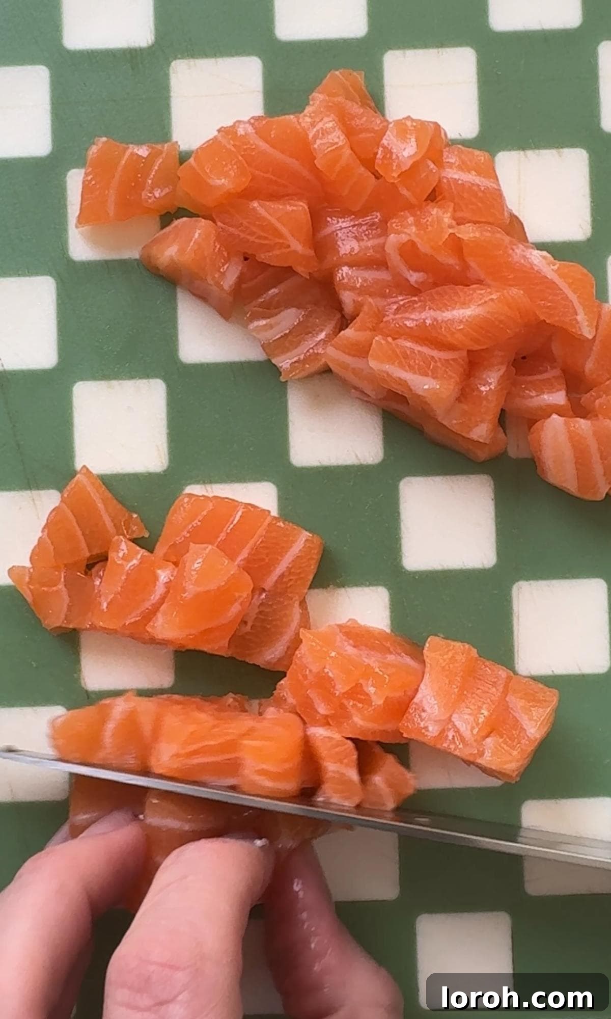 Slicing fresh, sushi-grade salmon into small, uniform cubes for a salmon sushi bowl.