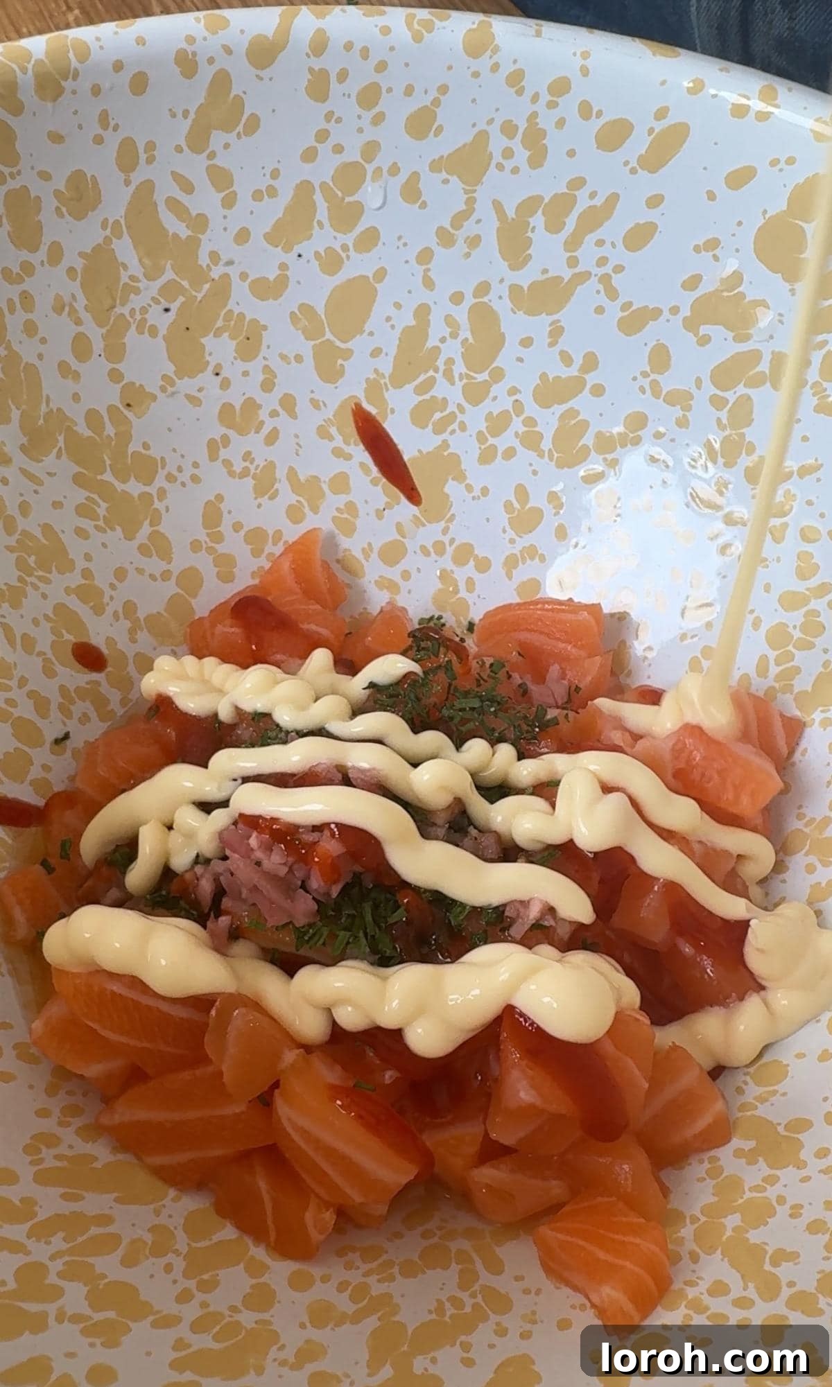 Mixing diced salmon with fresh herbs and a creamy sriracha-mayo dressing in a large bowl.