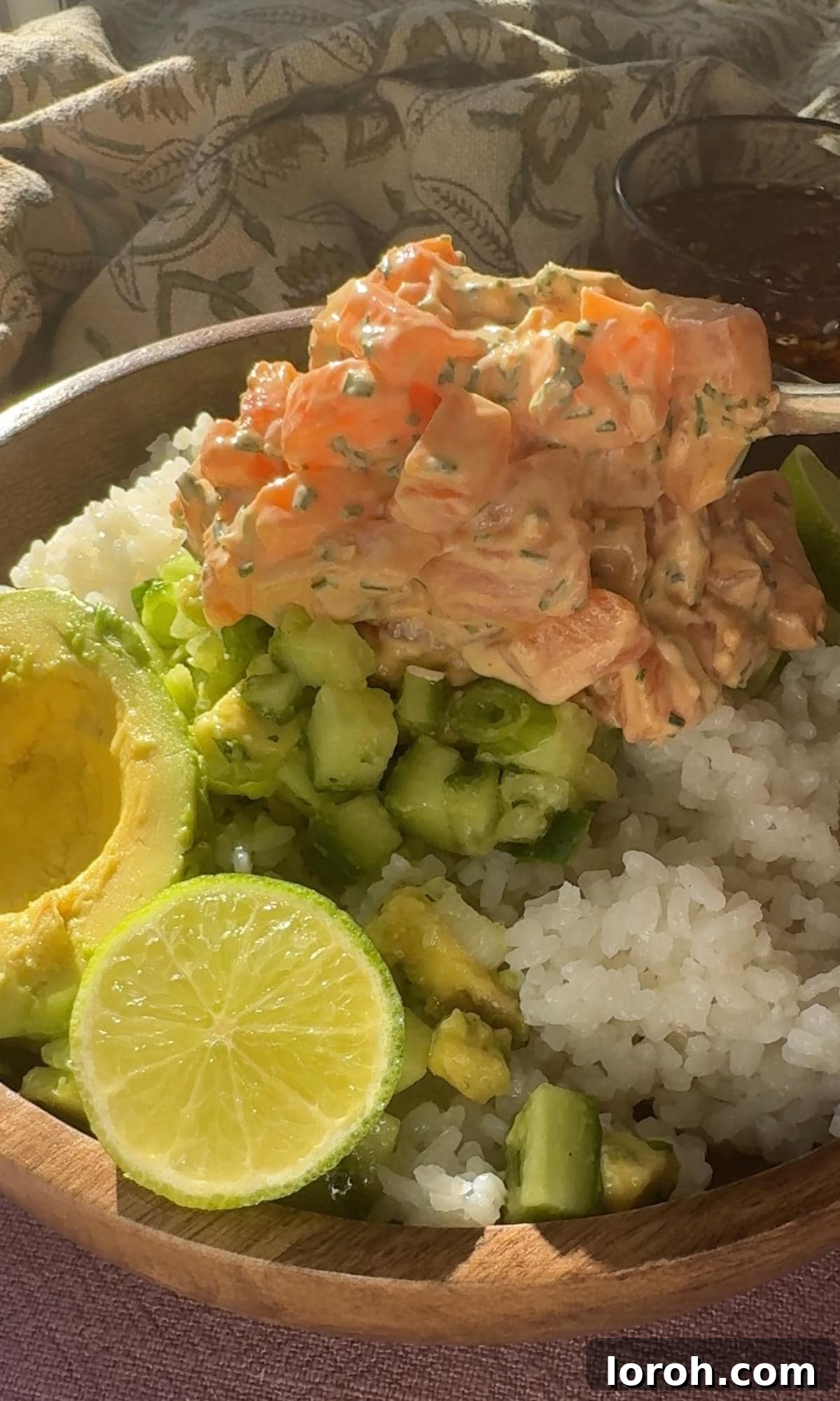 Assembling a salmon sushi bowl with seasoned rice, fresh vegetables, and spicy salmon mixture.
