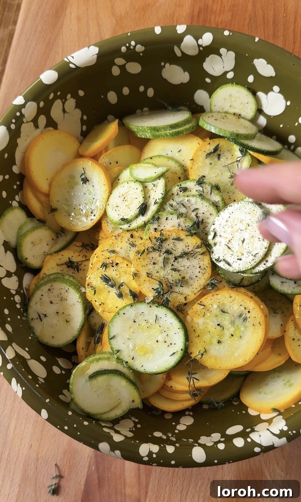 Seasoning thinly sliced zucchini with olive oil, salt, pepper, and fresh thyme leaves in a mixing bowl.