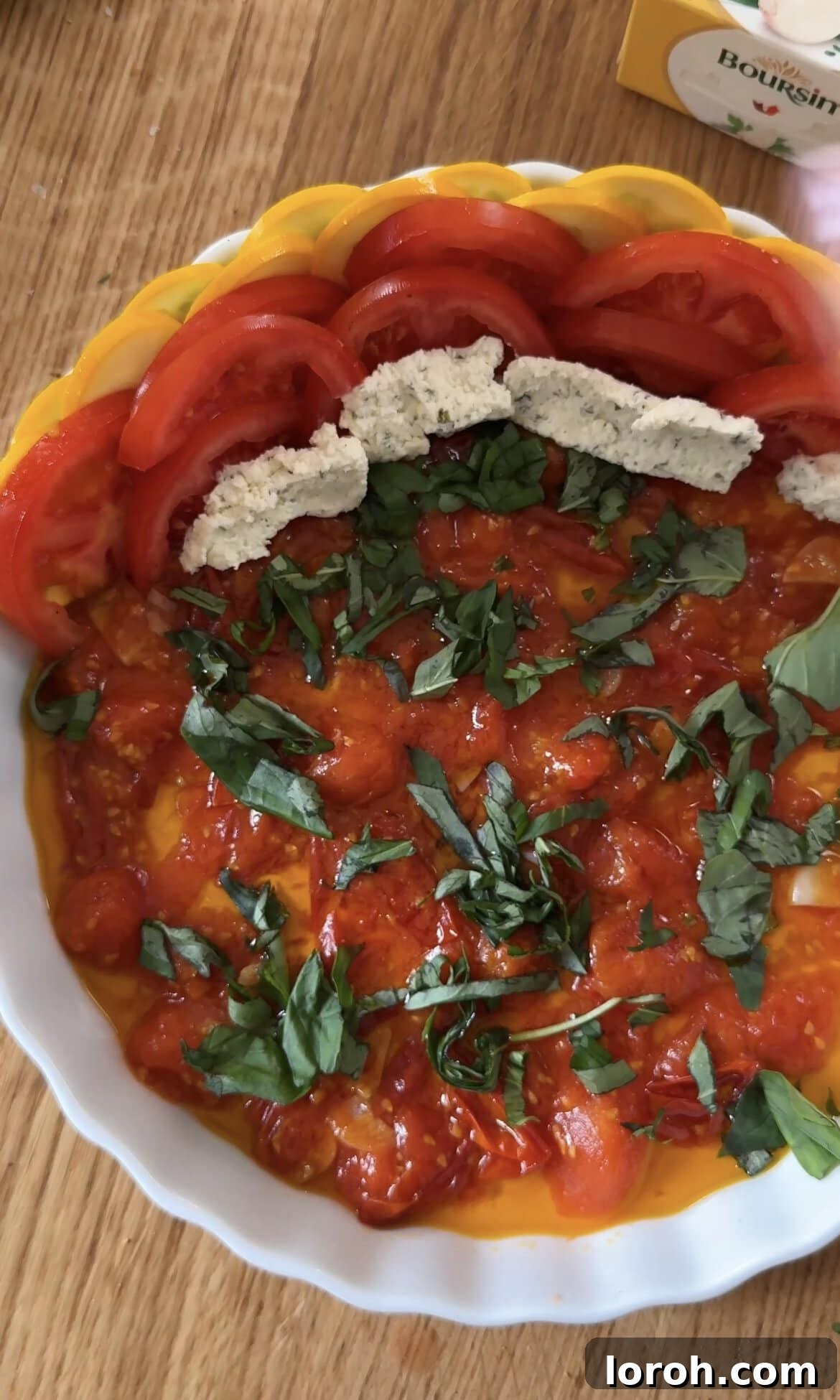 Carefully layering courgette slices, then spreading Boursin cheese onto tomato slices before placing them into the gratin dish.