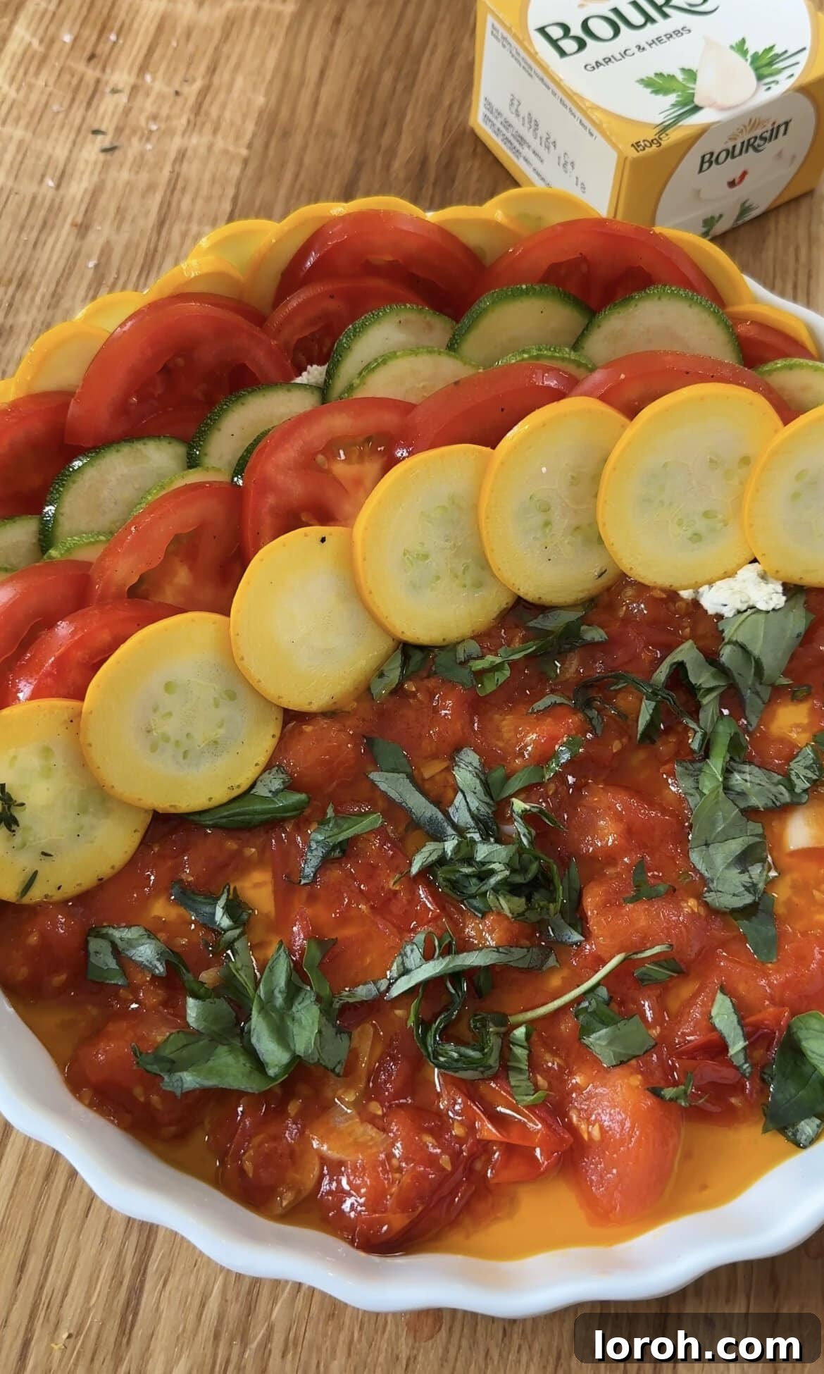 Continuing to layer courgette and Boursin-spread tomato slices in an alternating pattern to fill the gratin dish.