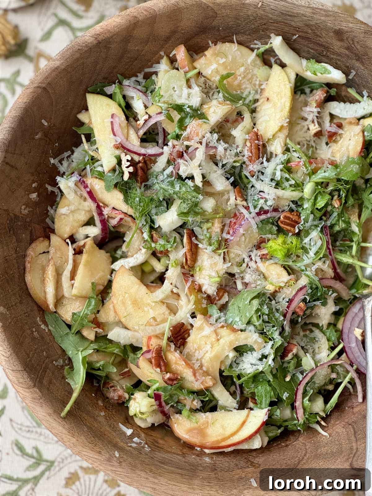 Detailed shot of fennel apple salad in a wooden bowl with grated cheese.