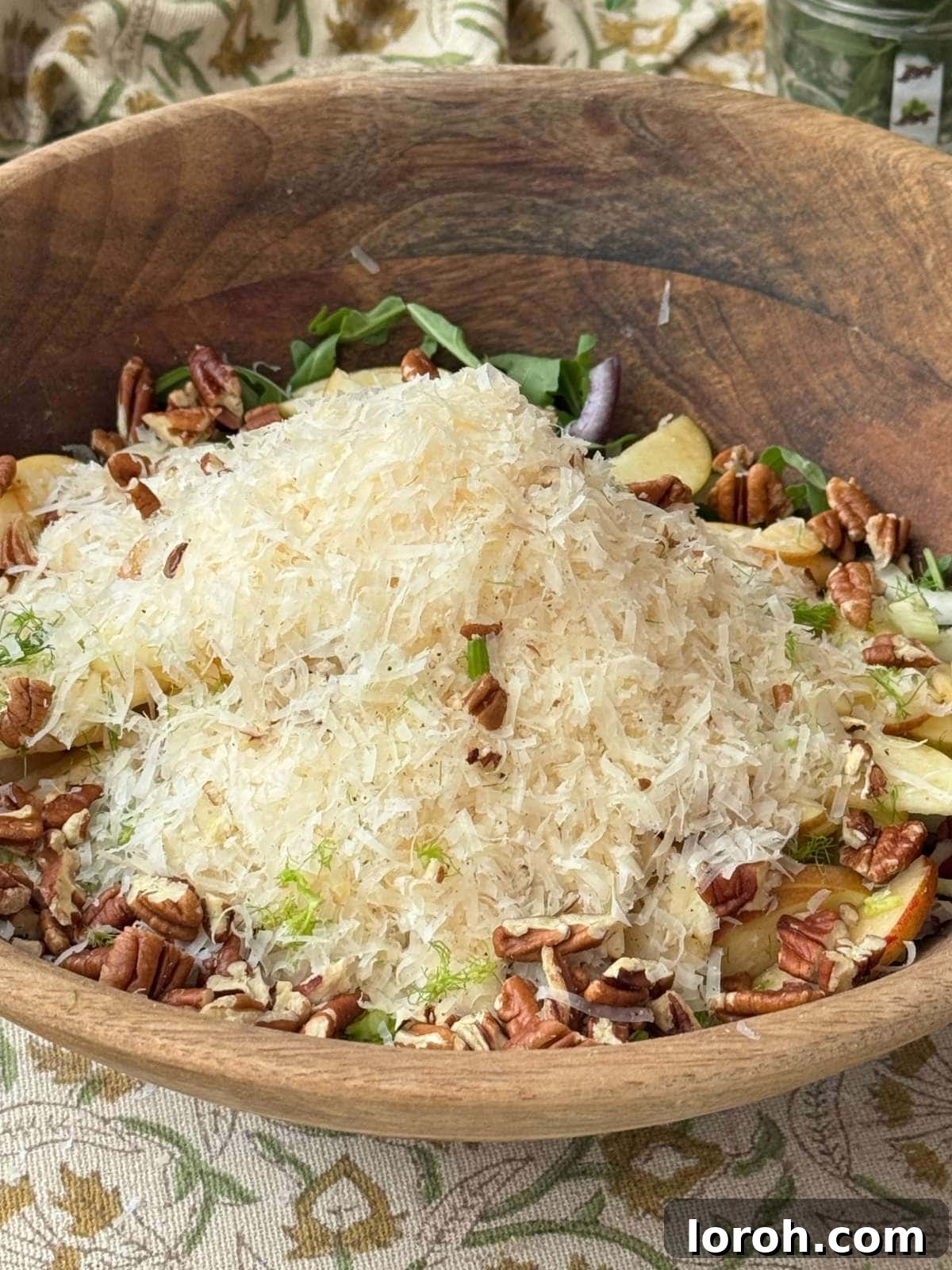 Close-up of the fennel apple salad in a wooden bowl, richly topped with grated Manchego.