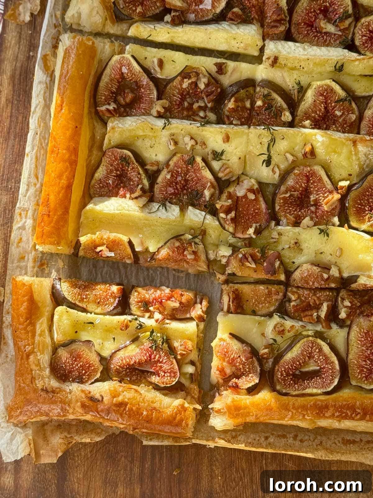 Fig and Brie Bliss Tart 2 A stunning savoury fig and brie tart, garnished with thyme and walnuts, resting on parchment paper.