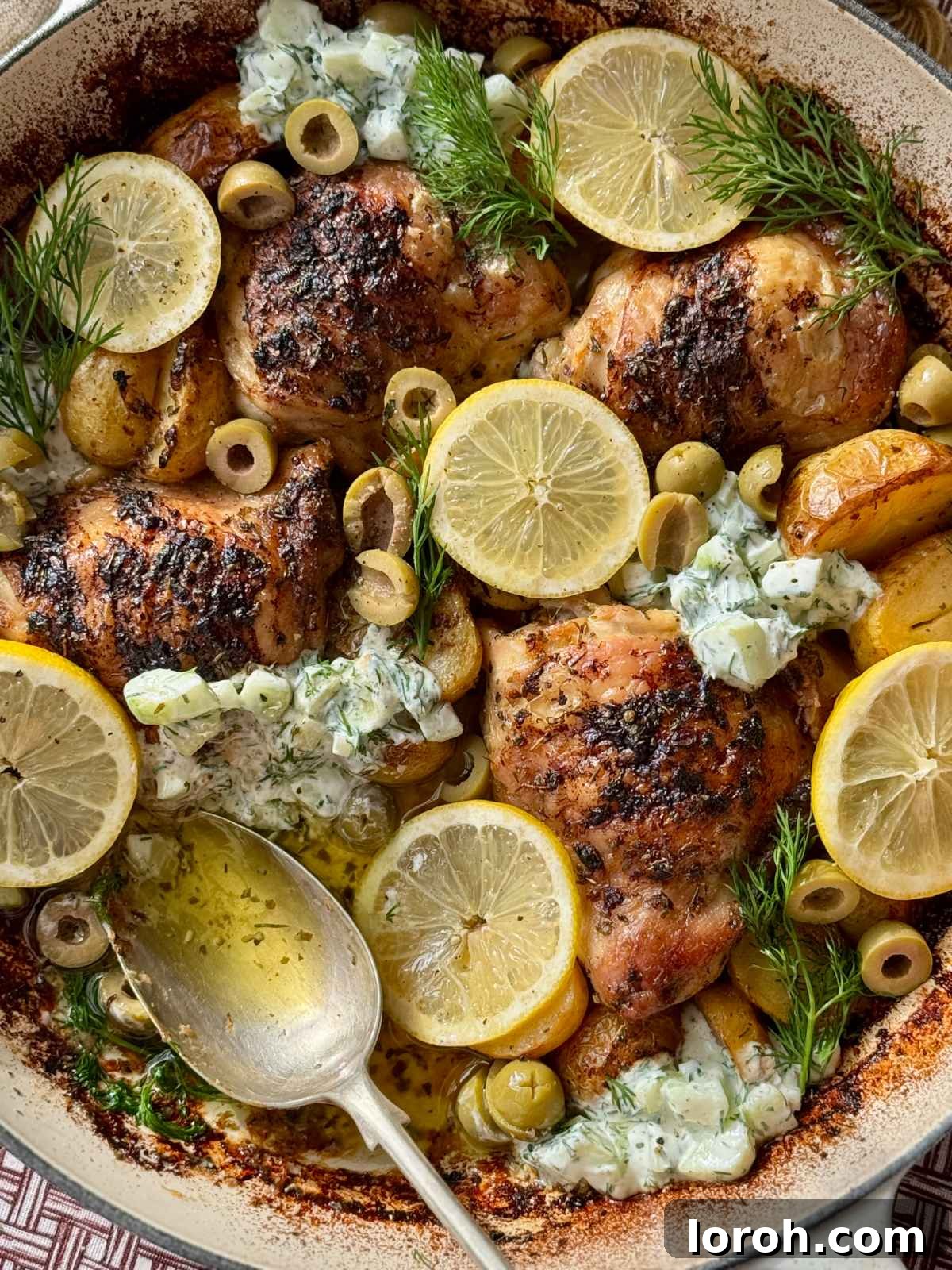 Greek chicken with lemon potatoes served in a white dish, garnished with fresh herbs and lemon slices.