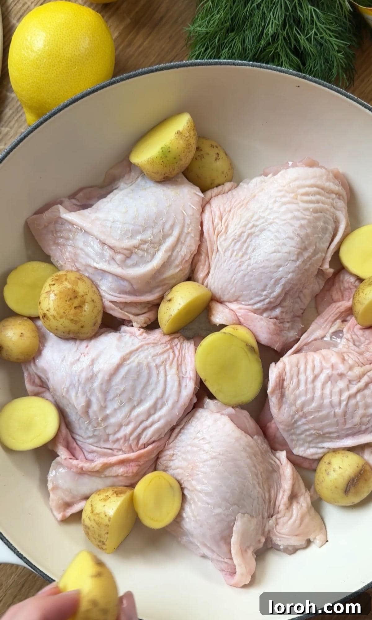 Arranging chicken thighs and halved potatoes in a large ovenproof dish.