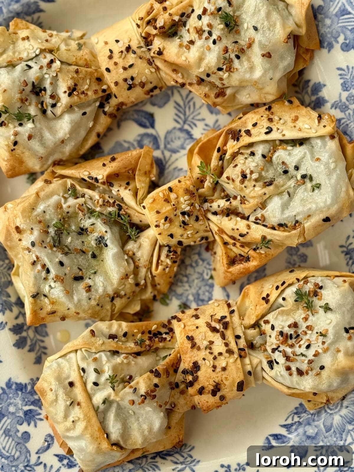 Crisp, golden spinach feta filo bows on a vibrant blue plate, garnished with sesame seeds.