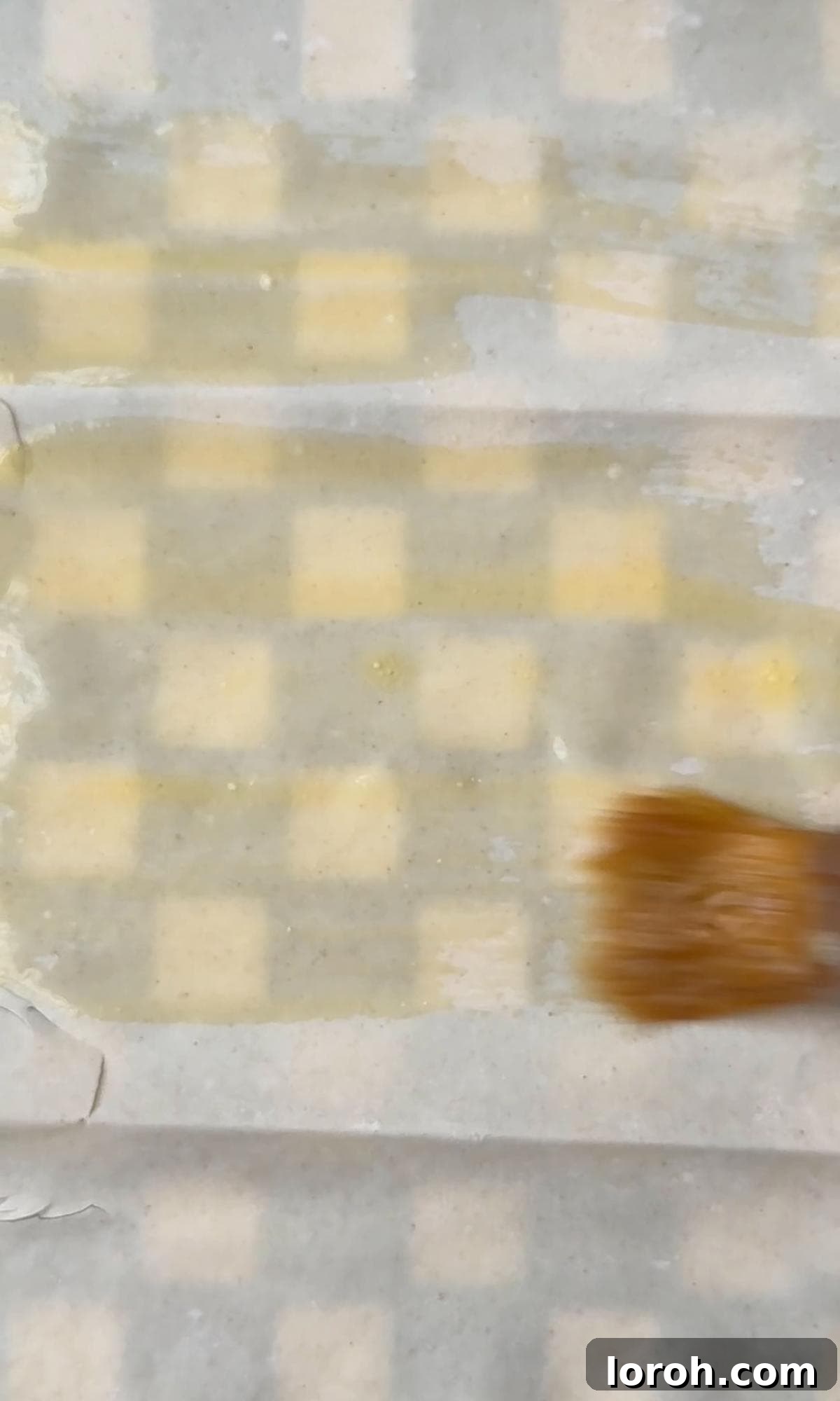 A hand brushing melted butter onto delicate filo pastry sheets.