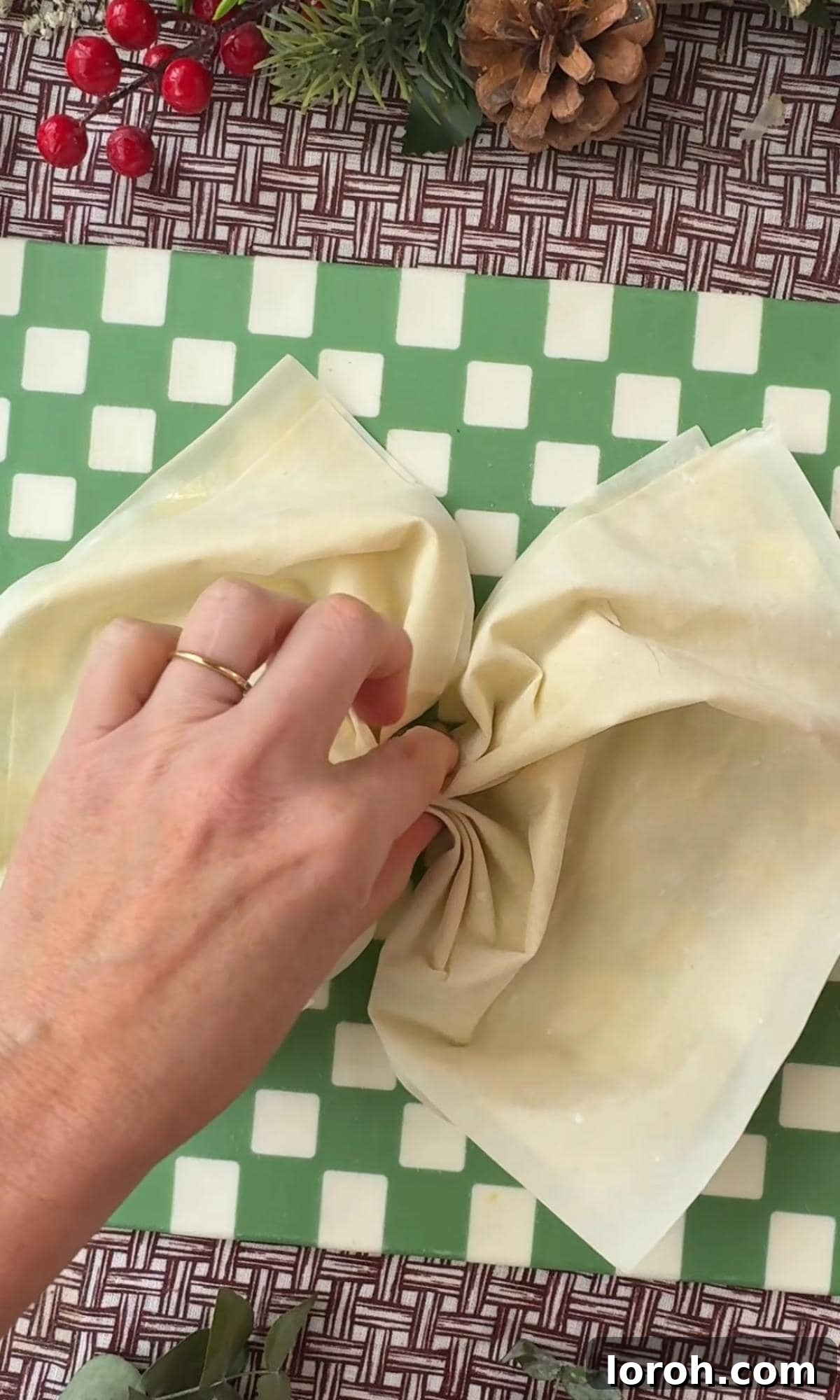 A hand gently pinching the middle of two layered filo pastry sheets to create a bow shape.