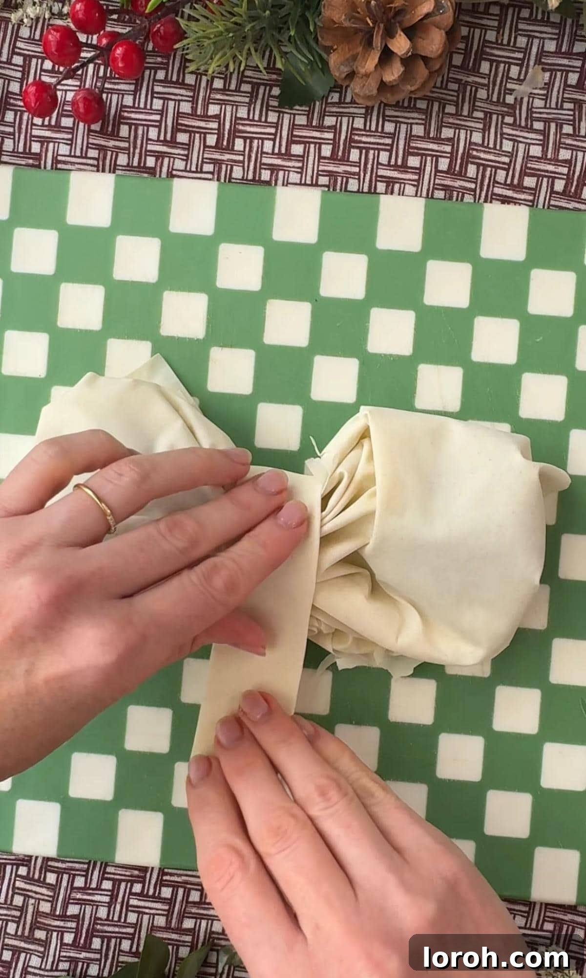 A thin strip of filo pastry being wrapped around the center of a bow to secure it.