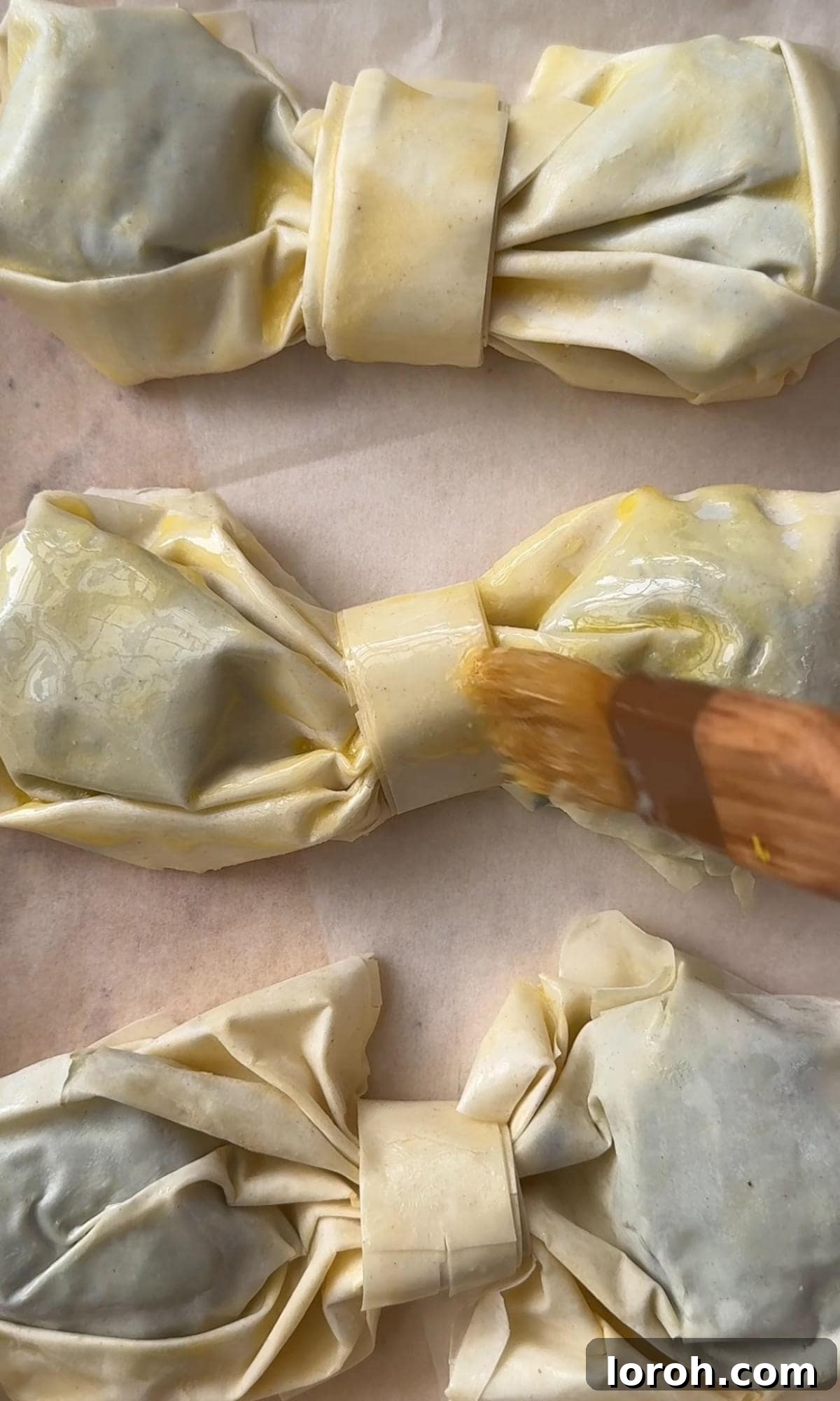 Finished filo bows arranged on a parchment-lined baking tray, ready for baking.