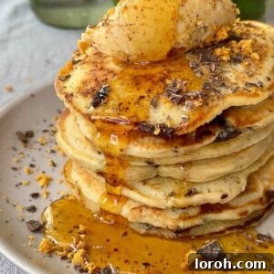 A generous stack of classic chocolate chip pancakes, drenched in golden syrup, ready to be enjoyed.
