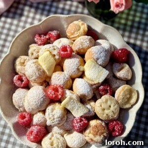 A bowl brimming with fluffy Poffertjes (Dutch mini pancakes), adorned with melting butter and fresh raspberries.