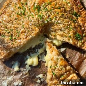 A beautifully sliced pithivier with a golden, flaky crust, revealing a savory ham and cheese filling, on a rustic wooden board.