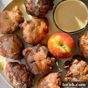 A plate of golden brown applesauce fritters, lightly glazed, accompanied by a fresh apple for a rustic touch.