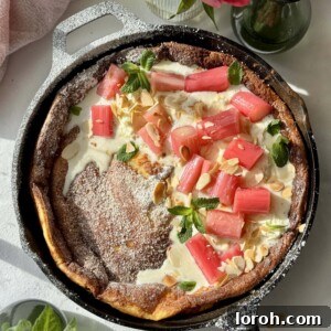 Golden brown Pannukakku (Finnish oven pancake) served in a cast iron pan, topped with whipped mascarpone cream and delicate poached rhubarb.