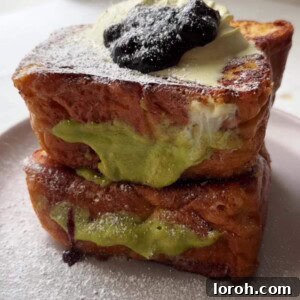 Golden brown brioche French toast filled with pistachio cream, topped with fresh blackcurrant jam for a delicious sweet and tangy contrast.