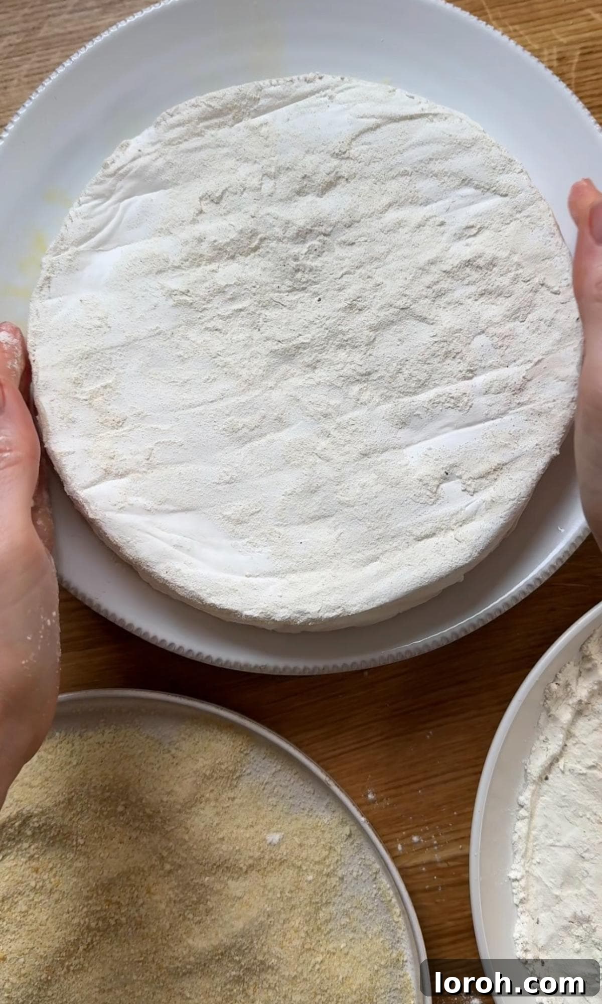 Dunking a wheel of brie first in flour, then in beaten eggs, as part of the breading process.
