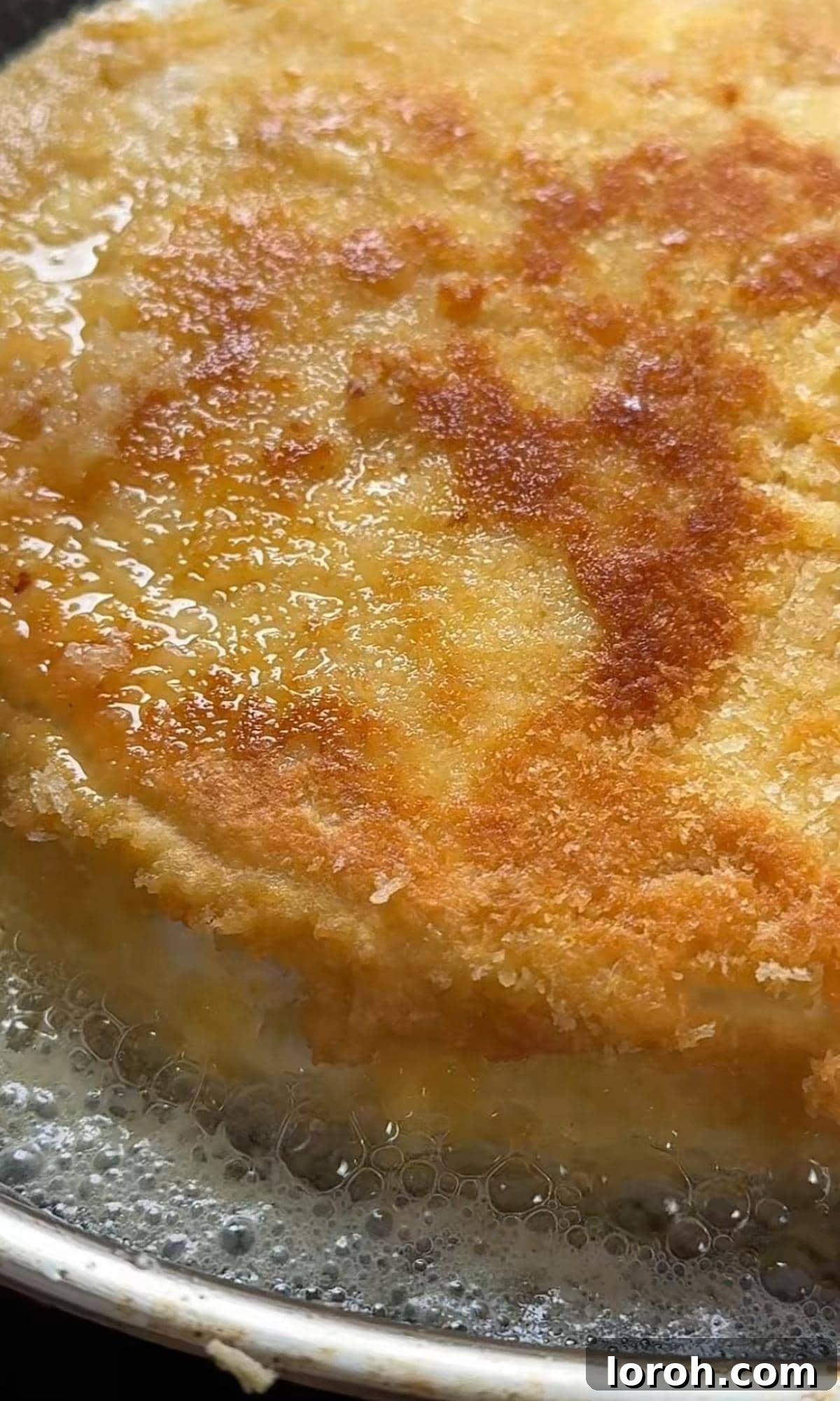Deep frying a golden-crusted brie wheel in a pan filled with hot oil.