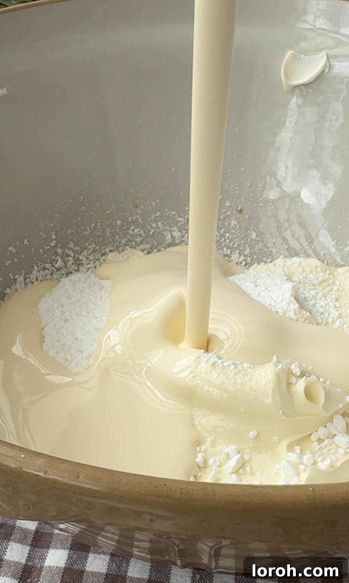 Adding double cream to a mixing bowl with cream cheese and icing sugar.