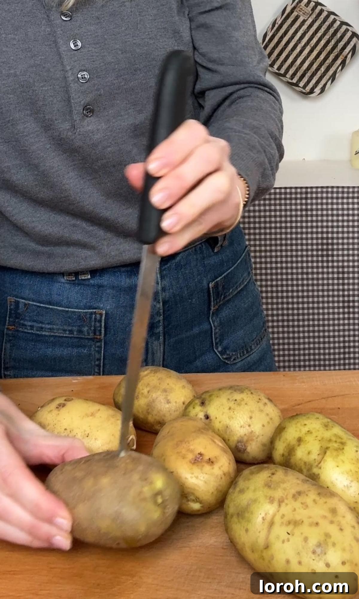 Piercing whole raw potatoes with a fork on a baking tray before roasting.