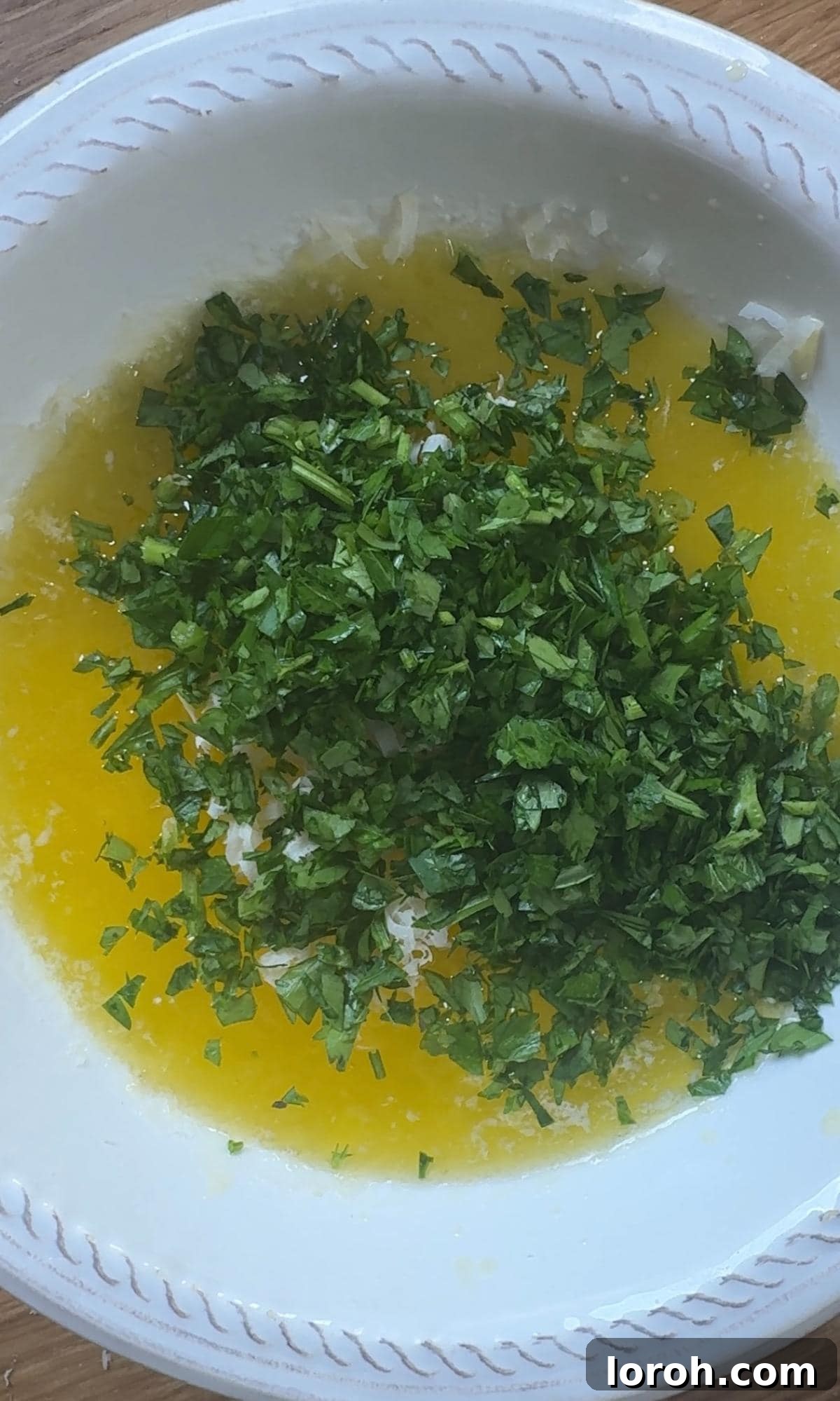 Mixing melted butter with finely chopped garlic and parsley in a small saucepan.