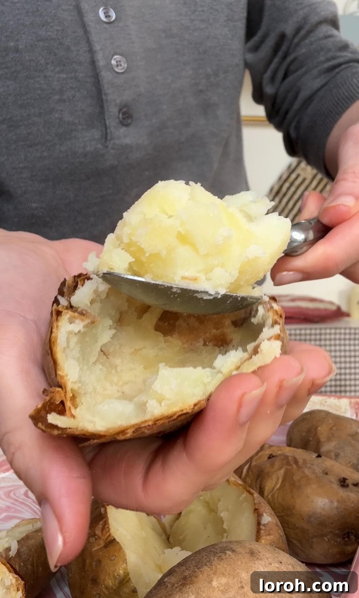 Scooping the fluffy flesh out of a roasted potato half into a mixing bowl.