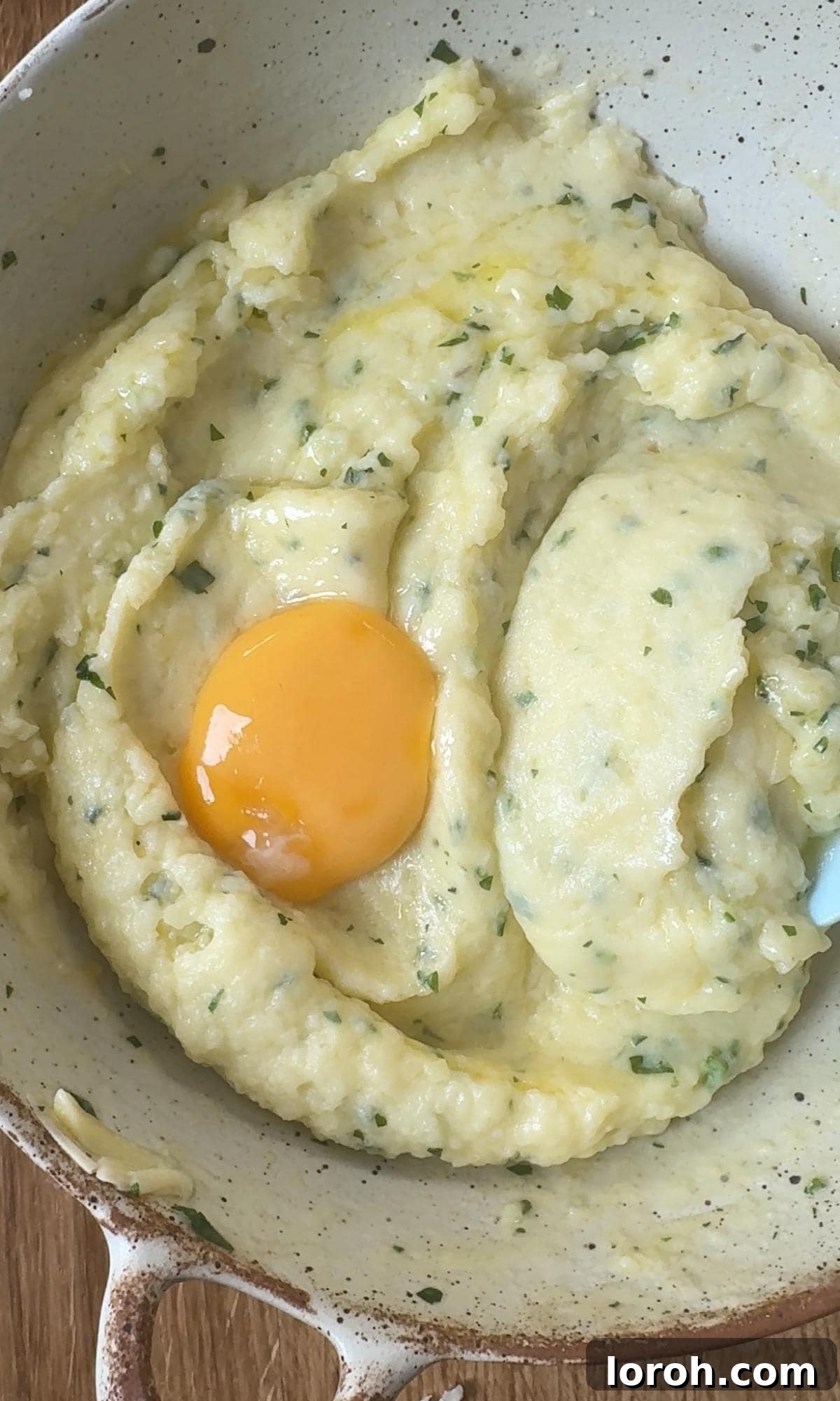 Adding an egg yolk to the mashed potatoes in a bowl, alongside melted butter and milk.