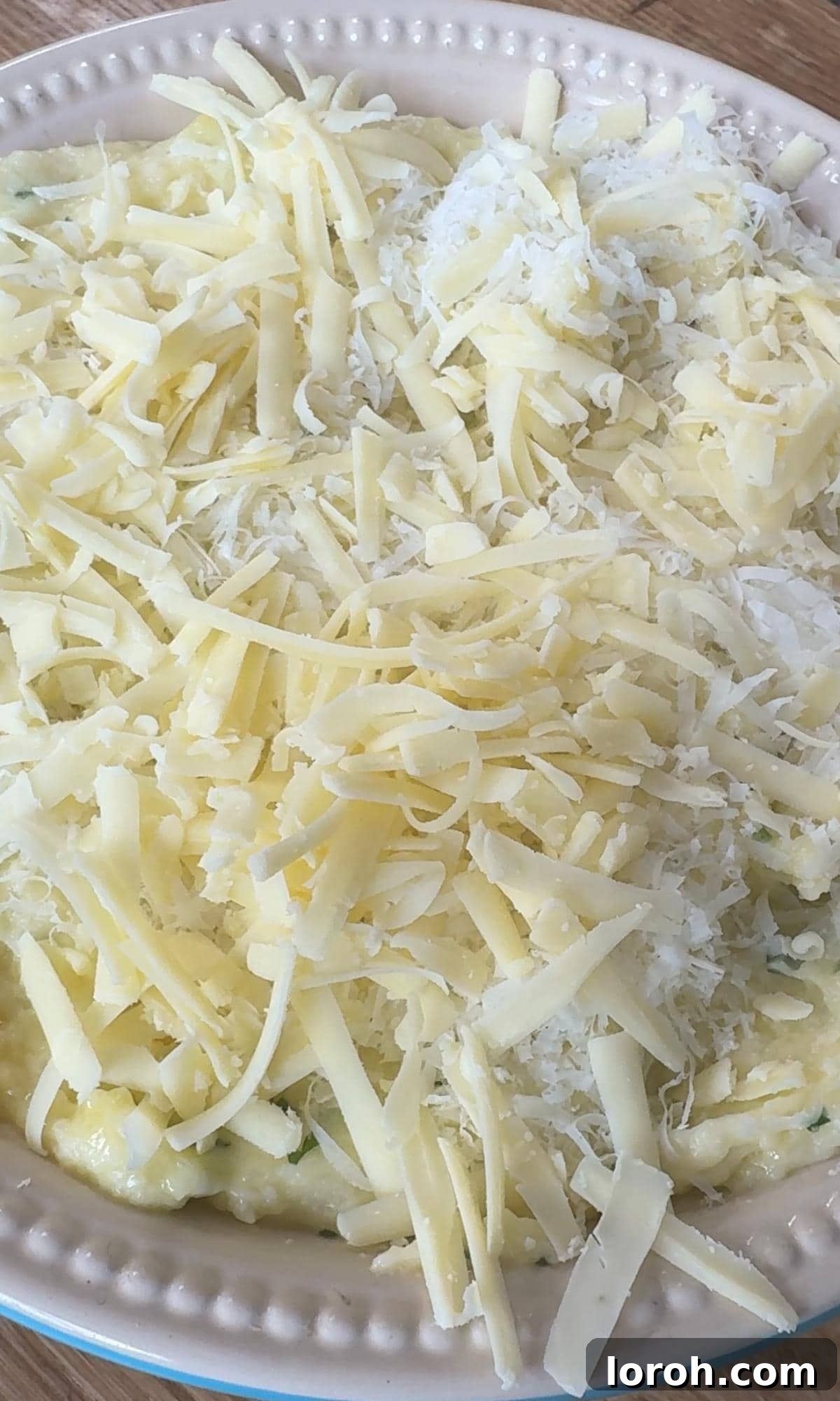 Spoon the creamy mashed potatoes into a small baking dish and creating ridges on the surface with a fork, then scattering grated cheese on top.