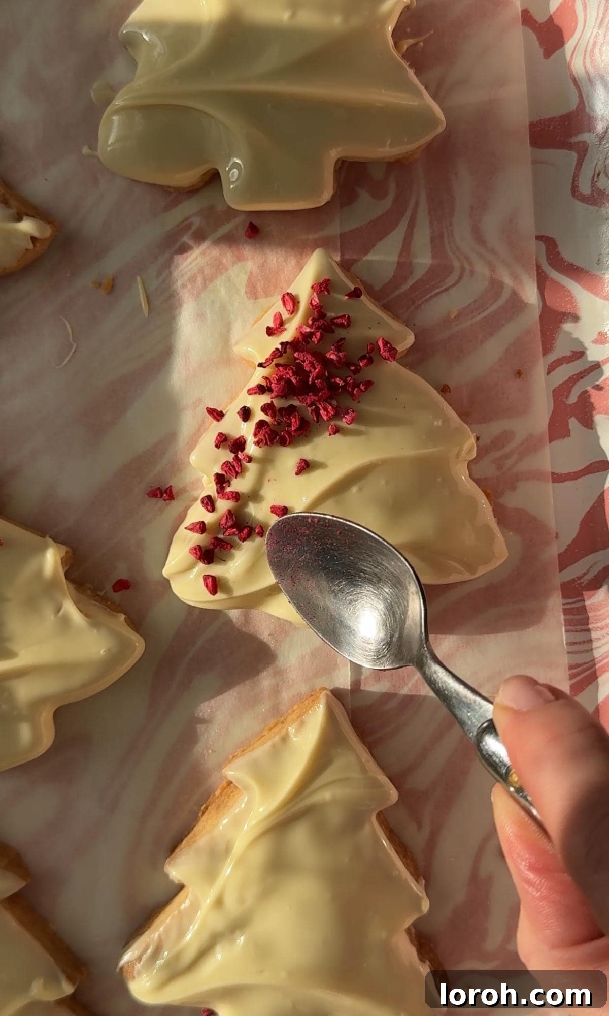 decorating Christmas tree cookies with crushed freeze-dried raspberries and pistachios.