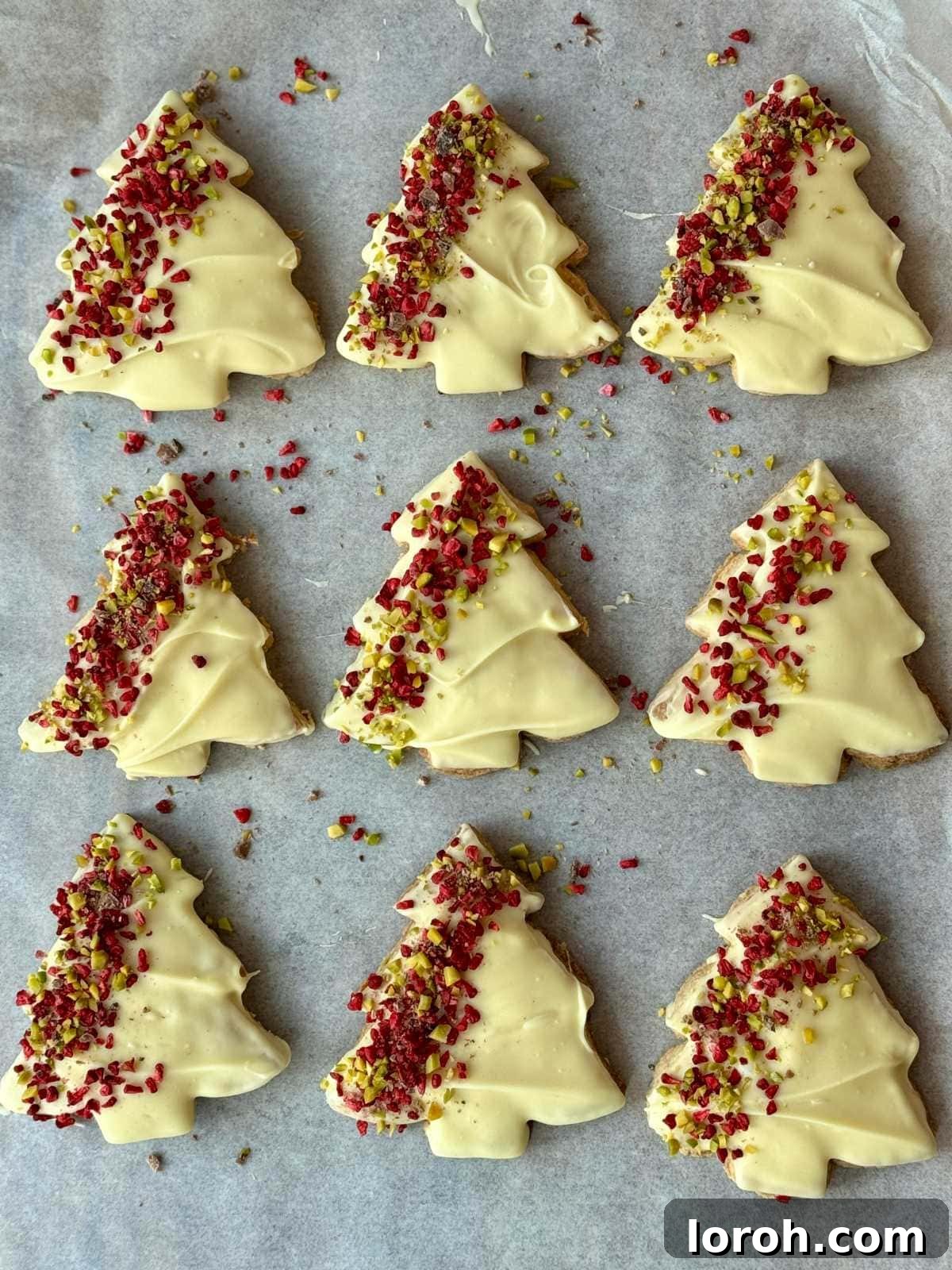 close up of several Christmas tree cookies decorated with white chocolate, raspberries, and pistachios.