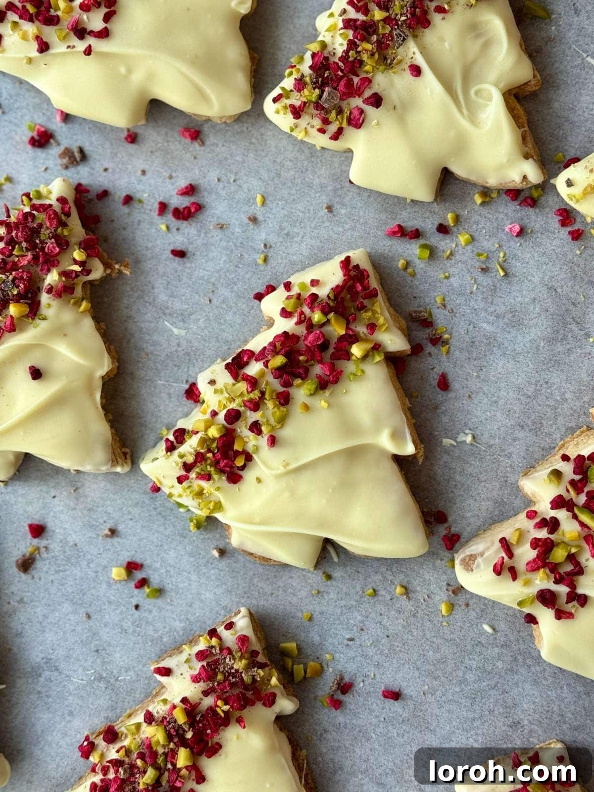 close up of decorated Christmas tree cookies on a white baking tray.