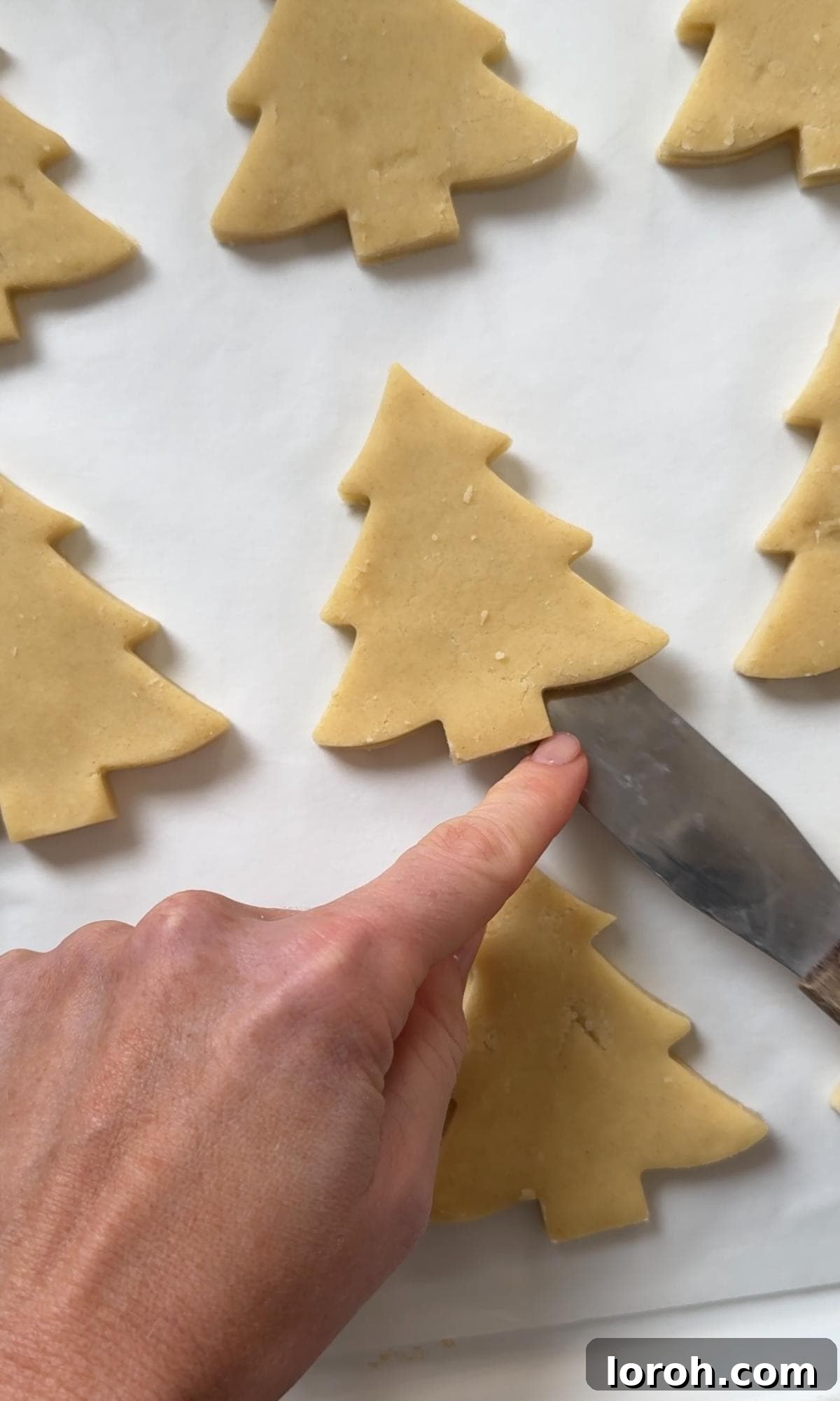 laying Christmas tree cookies on a lined baking sheet before baking.