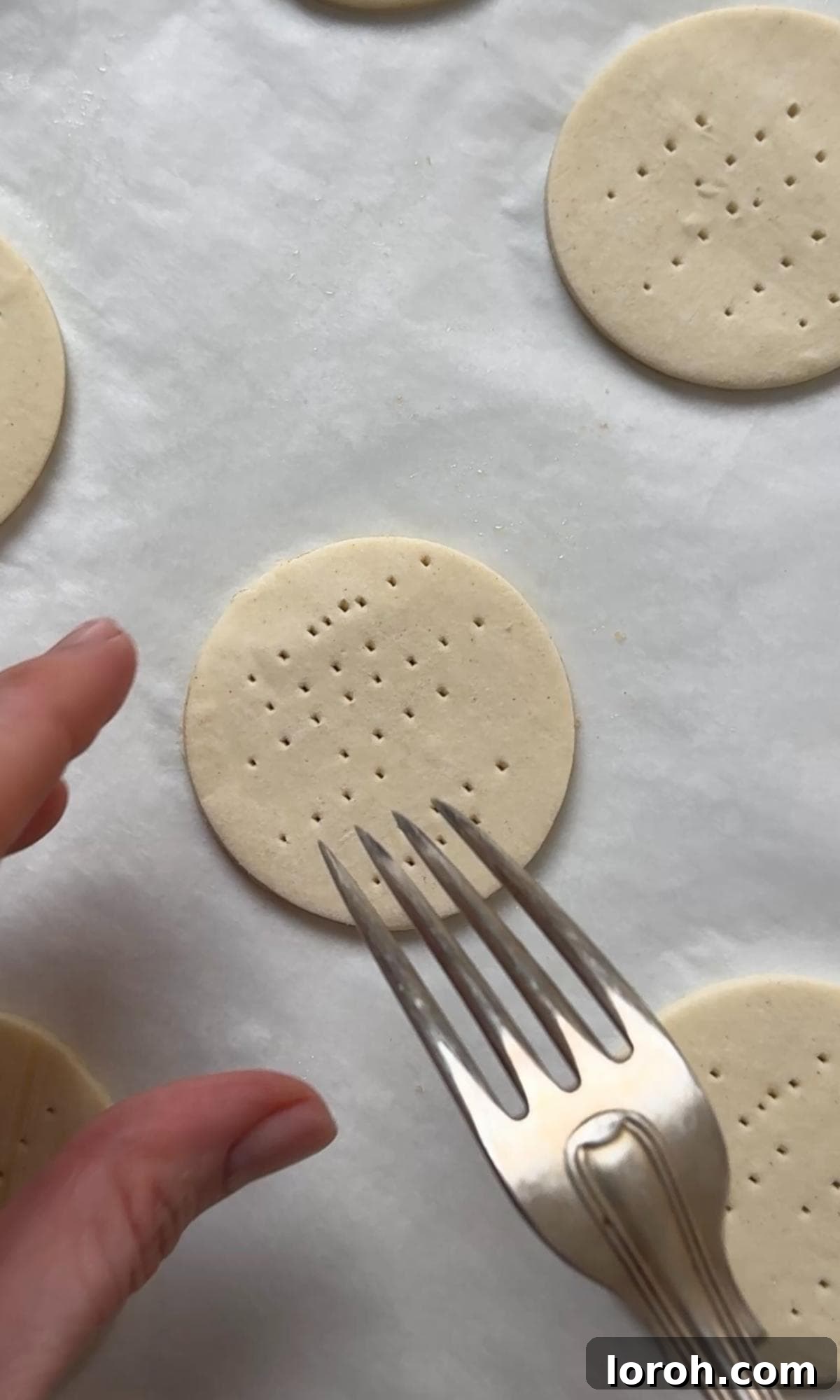A fork gently pricking the centers of round puff pastry bases on a baking sheet to prepare them for baking.