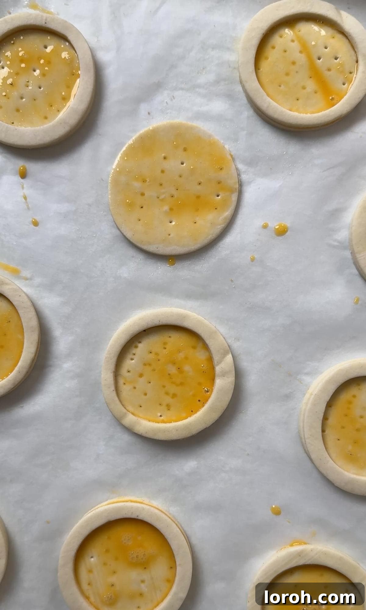 A pastry brush applying an egg wash to the assembled puff pastry cases before baking.