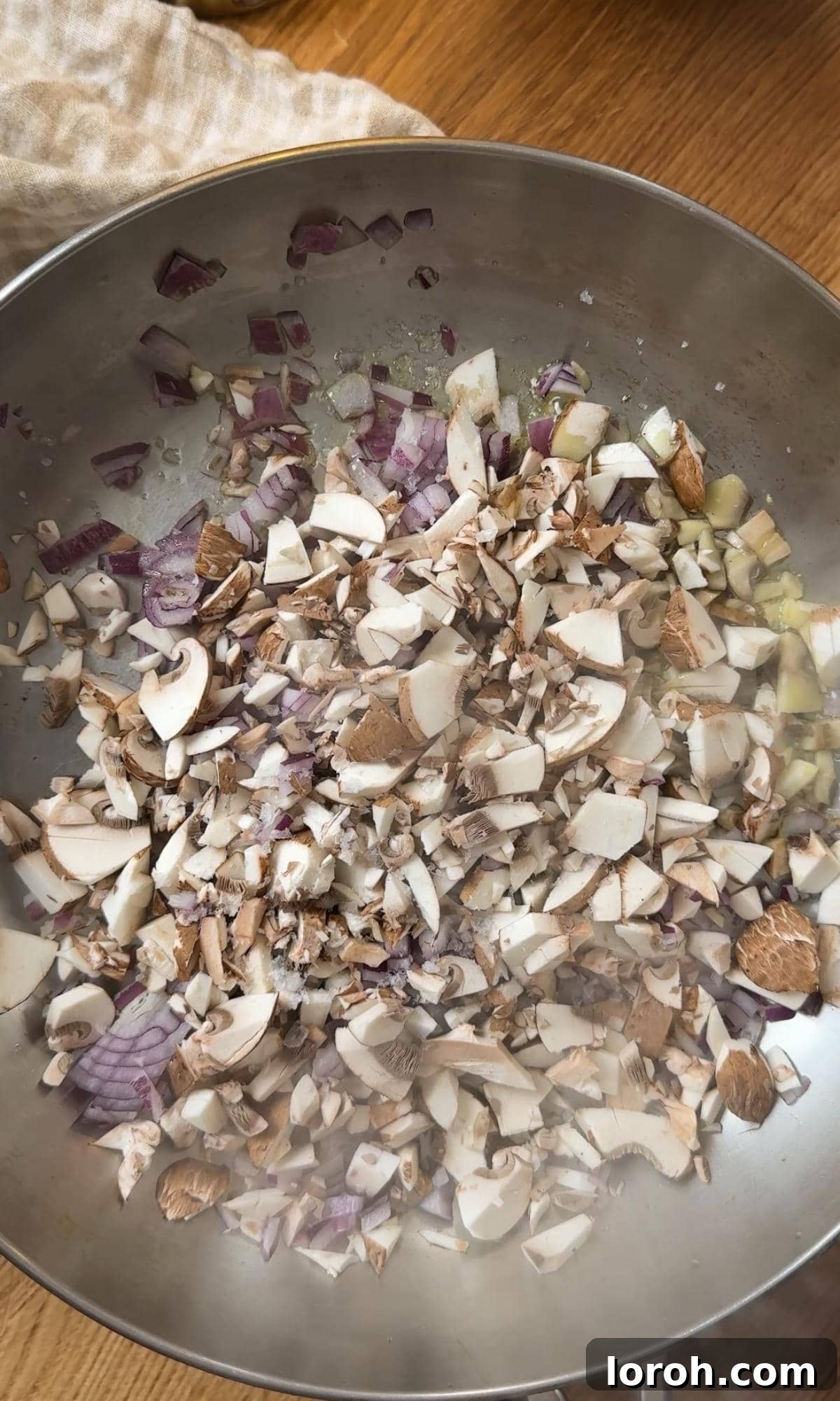 Finely chopped mushrooms being added to a hot pan with sautéed onions, ready to cook for the vol-au-vent filling.