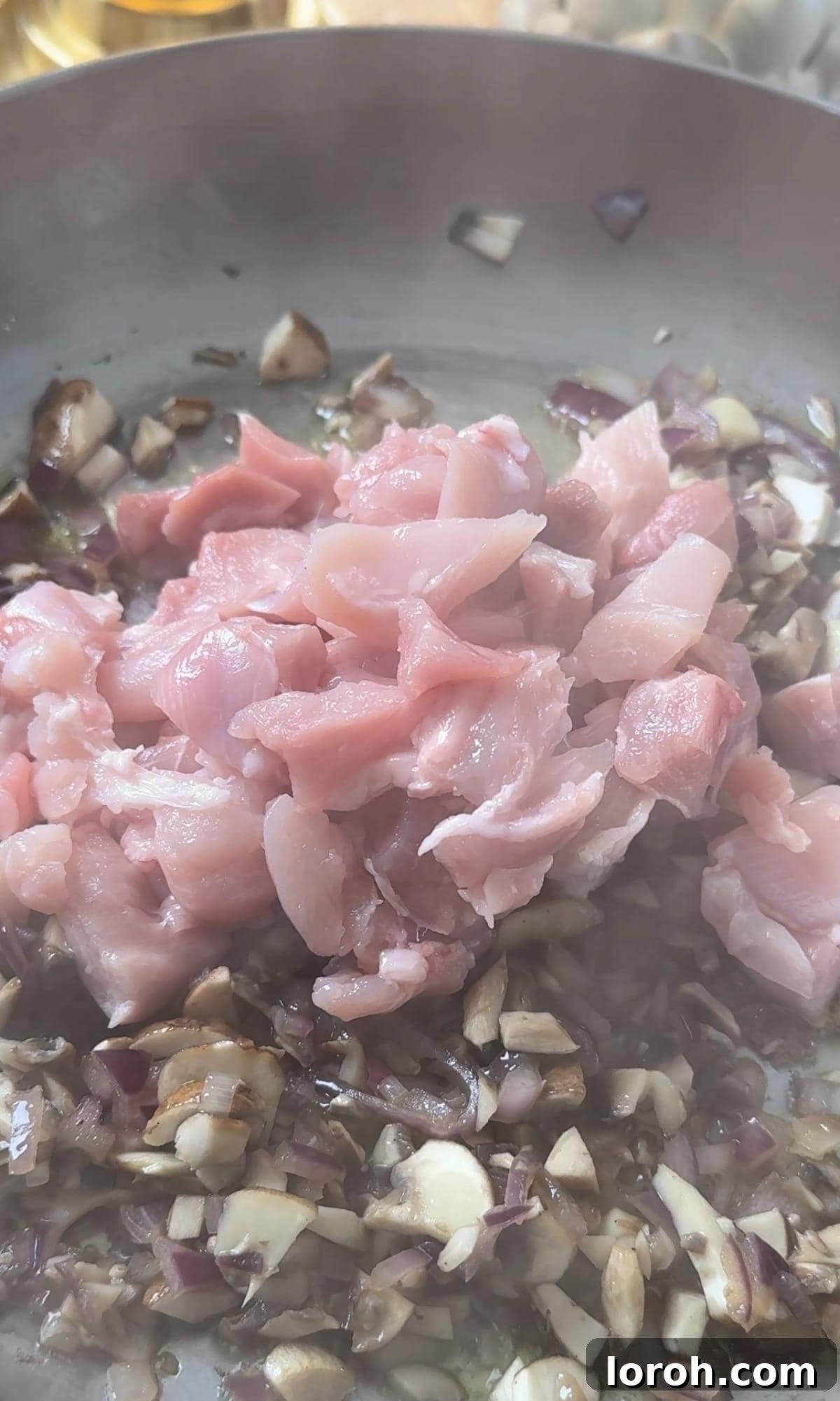 Finely chopped chicken thigh being cooked in a pan with sautéed onions and mushrooms, forming the base of the creamy filling.