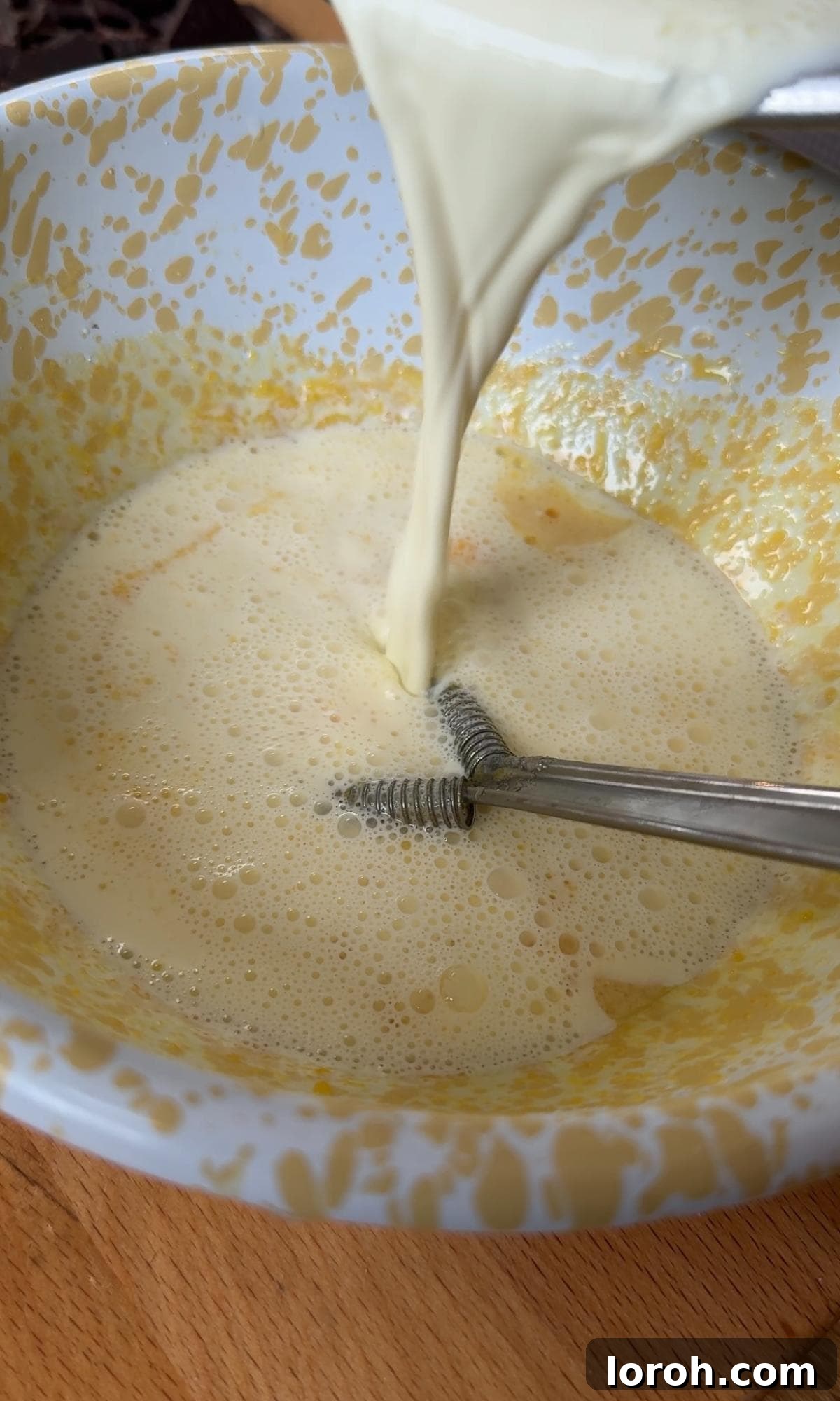 Velvet Chocolate Budino 5 Carefully pouring hot cream into the whisked egg yolk and sugar mixture to temper the eggs, ensuring constant stirring.