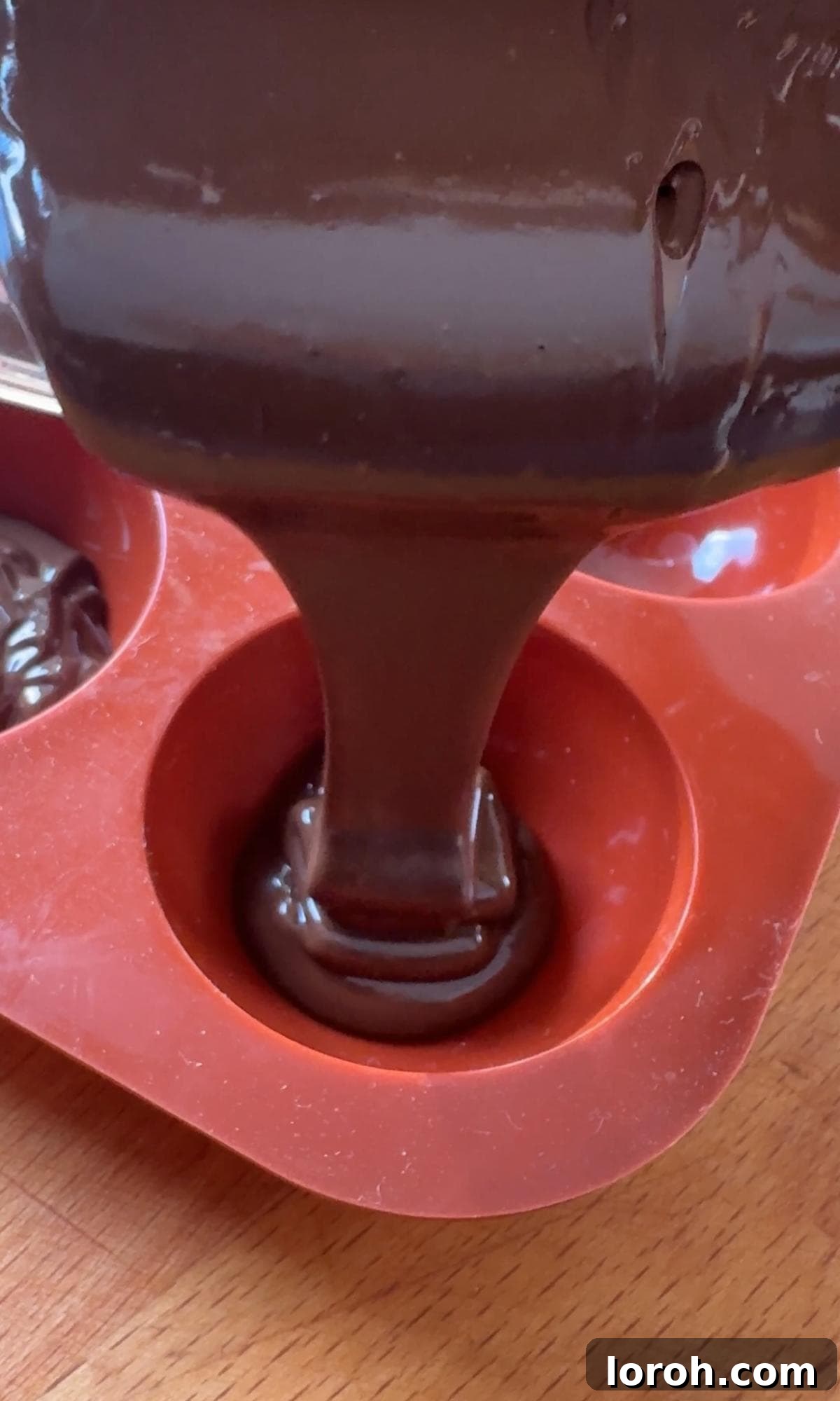 A hand pouring melted chocolate into a semi-sphere silicone mould.