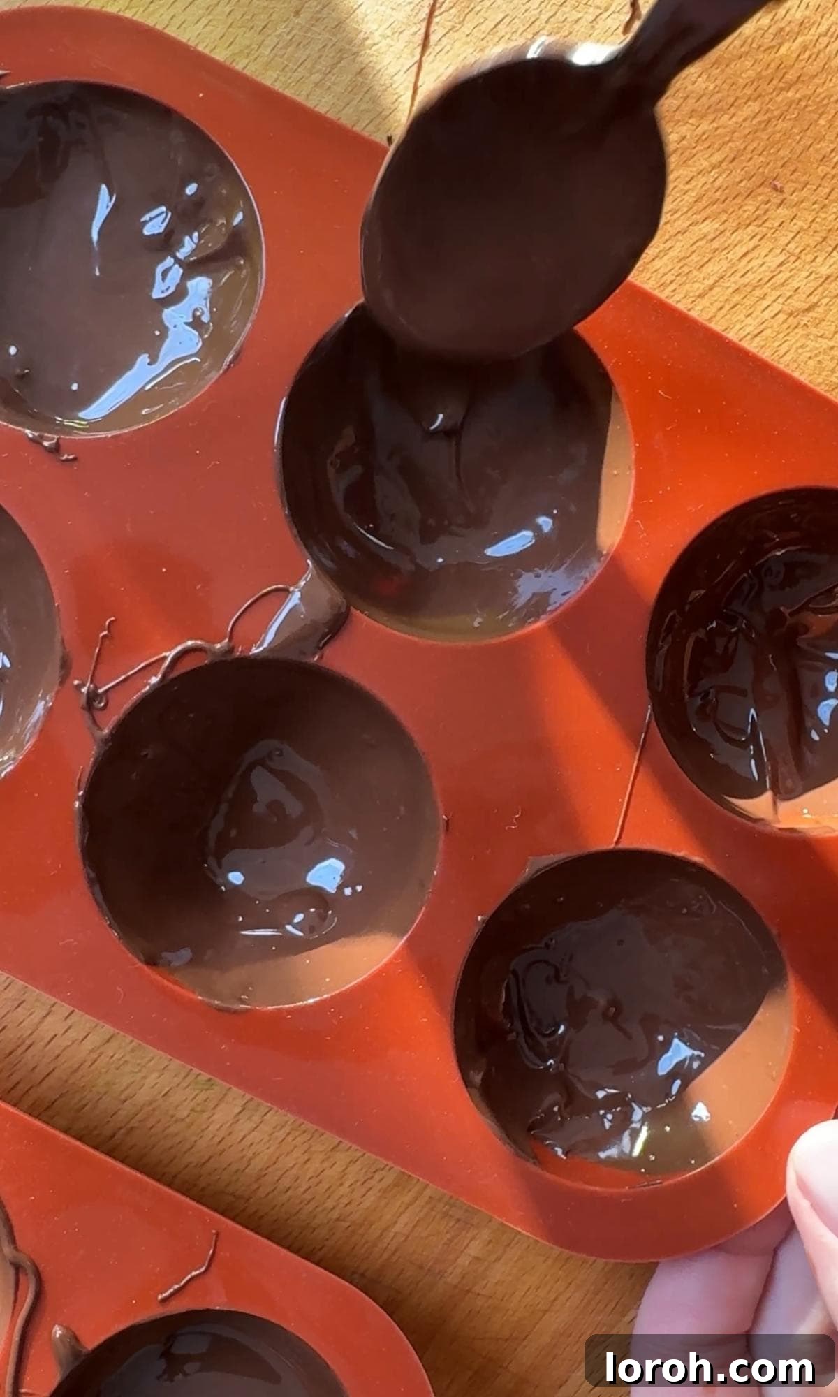 A spoon smoothing melted chocolate around the edges of a silicone mould.