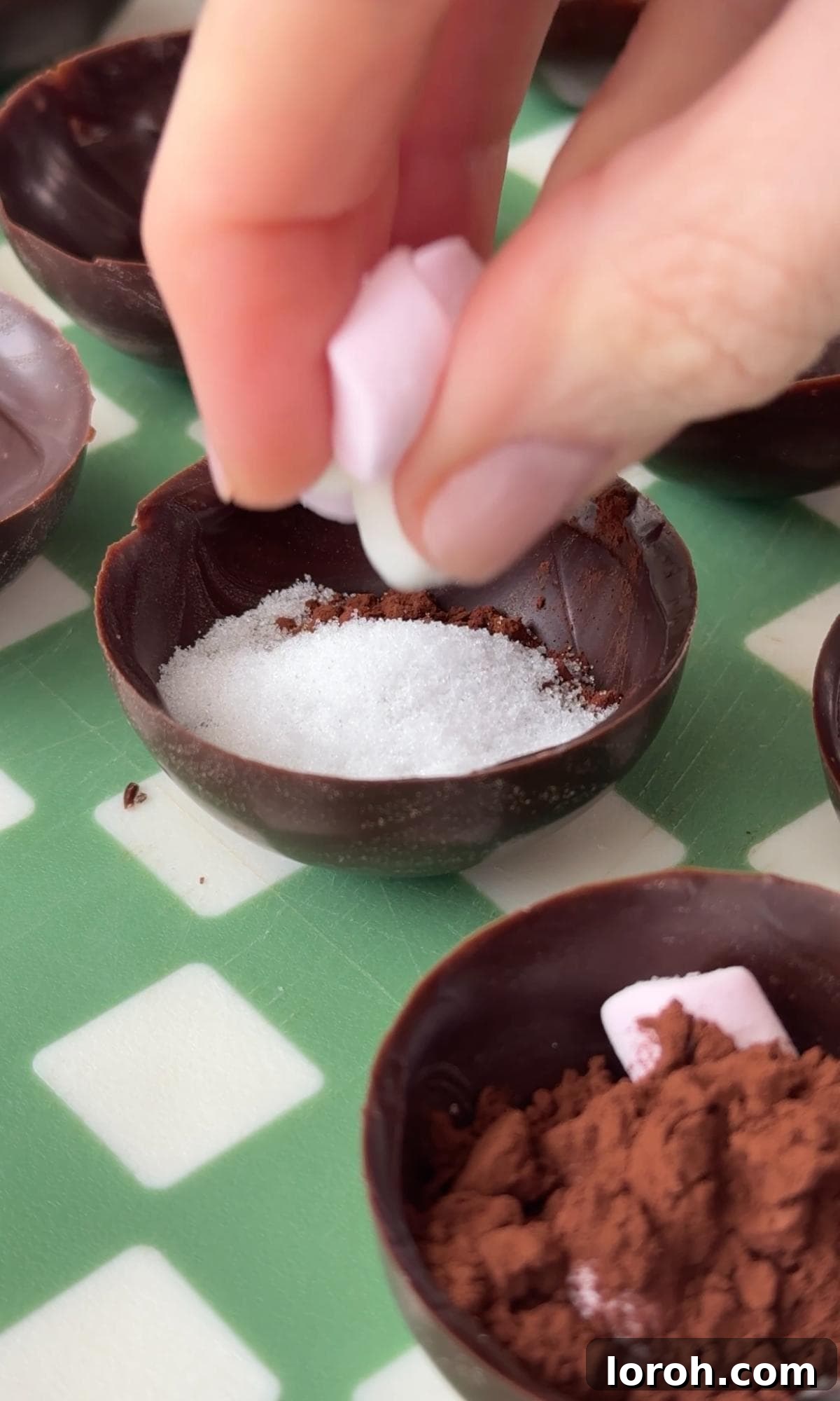 Filling four chocolate semi-spheres with cocoa powder, sugar, and mini marshmallows.